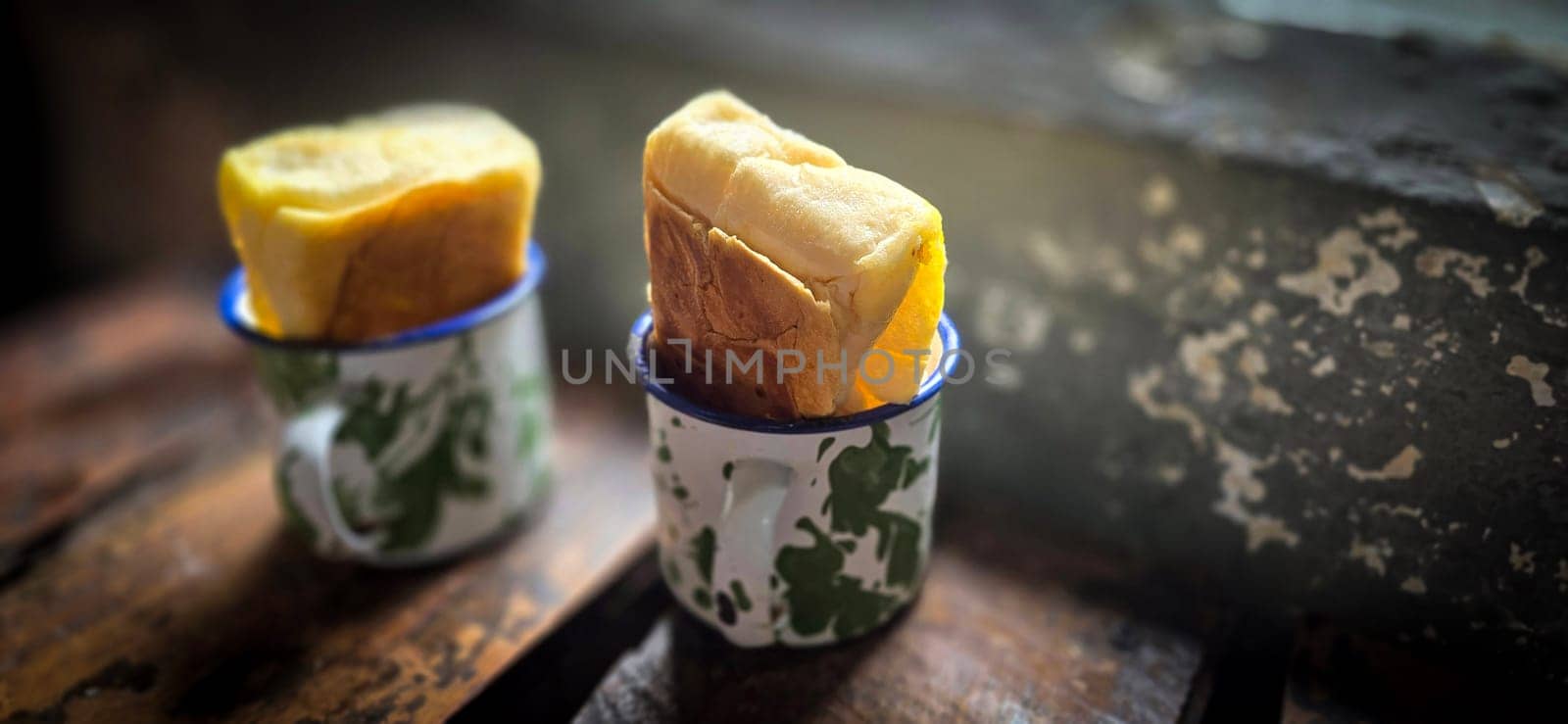 Ice chocolate drink on a vintage Indonesian iron mug with random green pattern called Blirik cup or cangkir Blirik on bokeh background along with chocolate filling bread on a cafe in Bogor