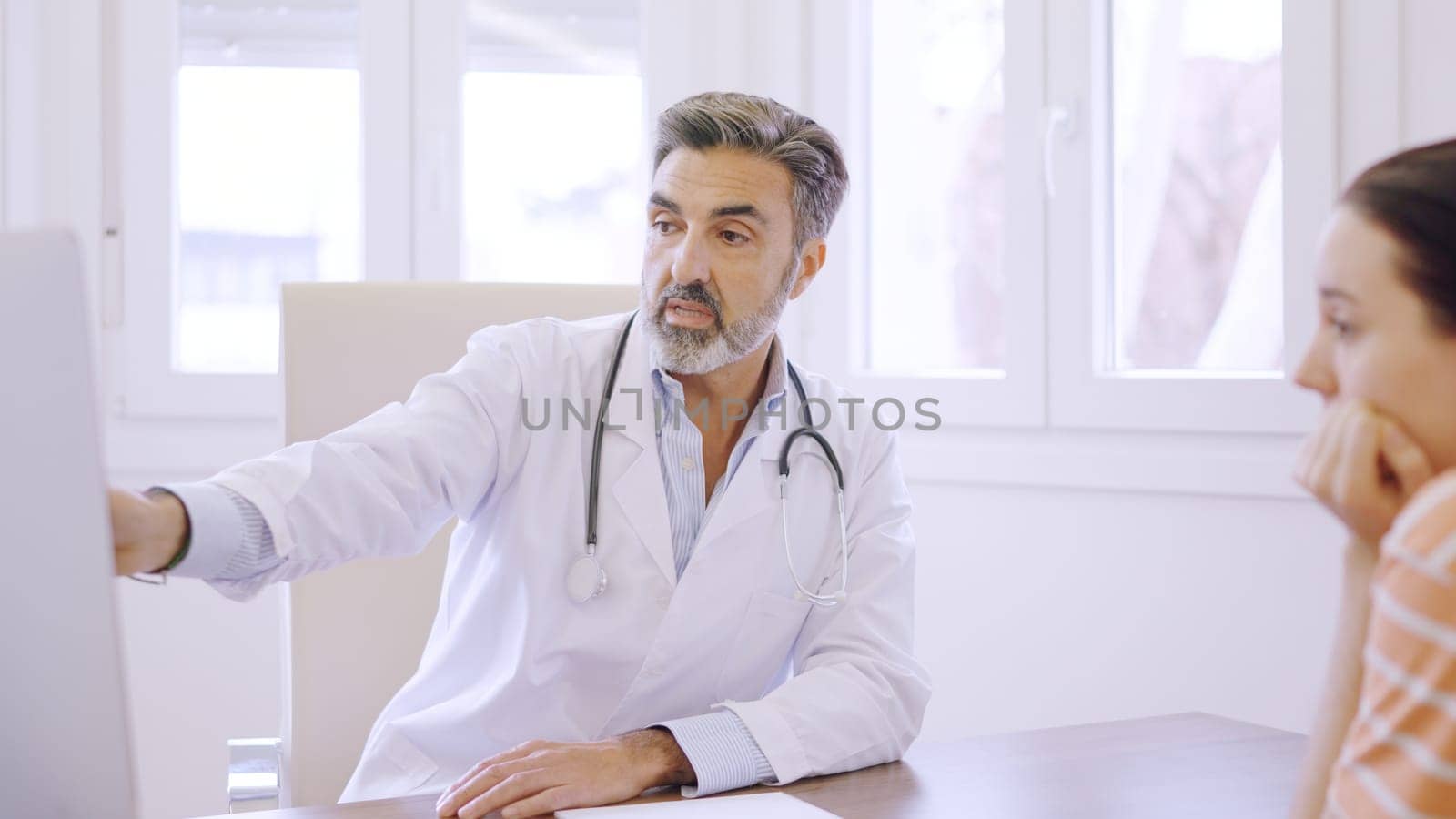Mature doctor pointing to computer screen giving an explanation to a patient