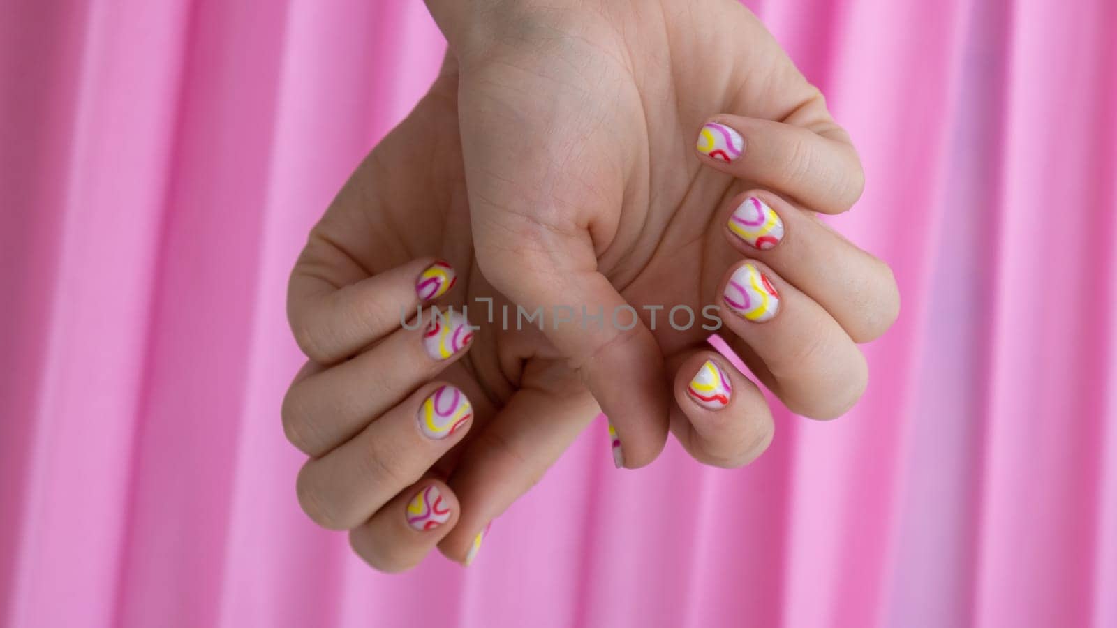Woman manicured hands, stylish summer colorful nails on pink background. Closeup of manicured nails of female hand. Summer style of nail design concept. Beauty treatment.