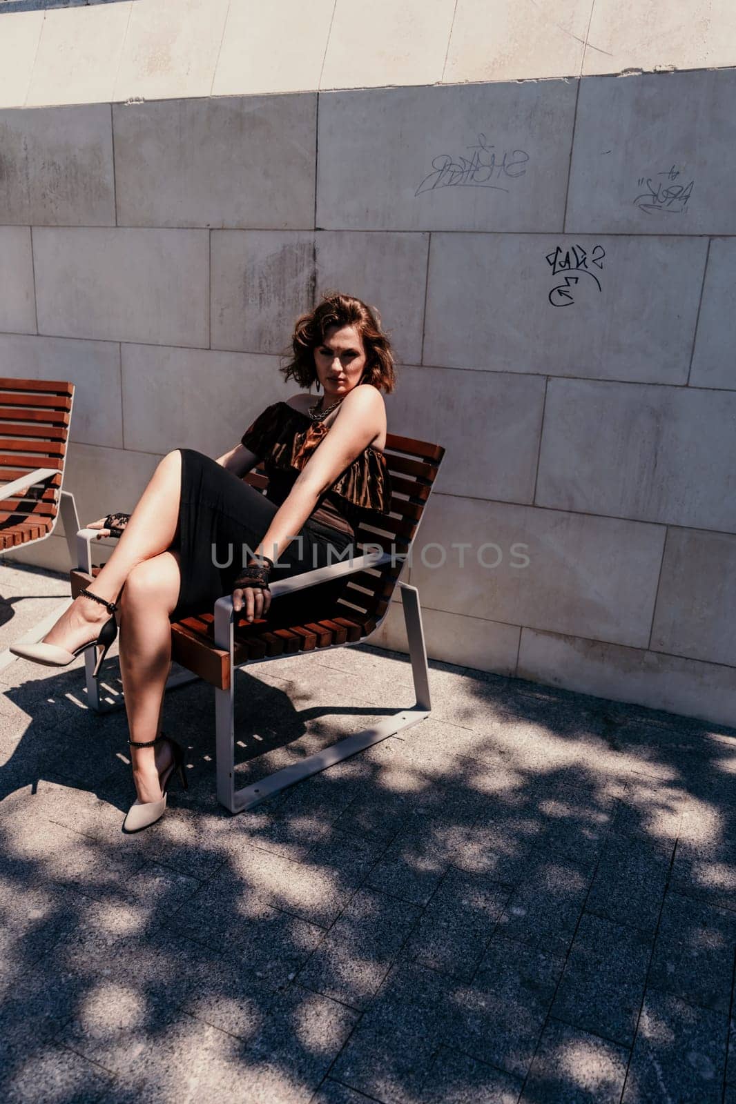 Portrait of a woman on the street. An attractive woman in a black dress is sitting on a bench outside. by Matiunina