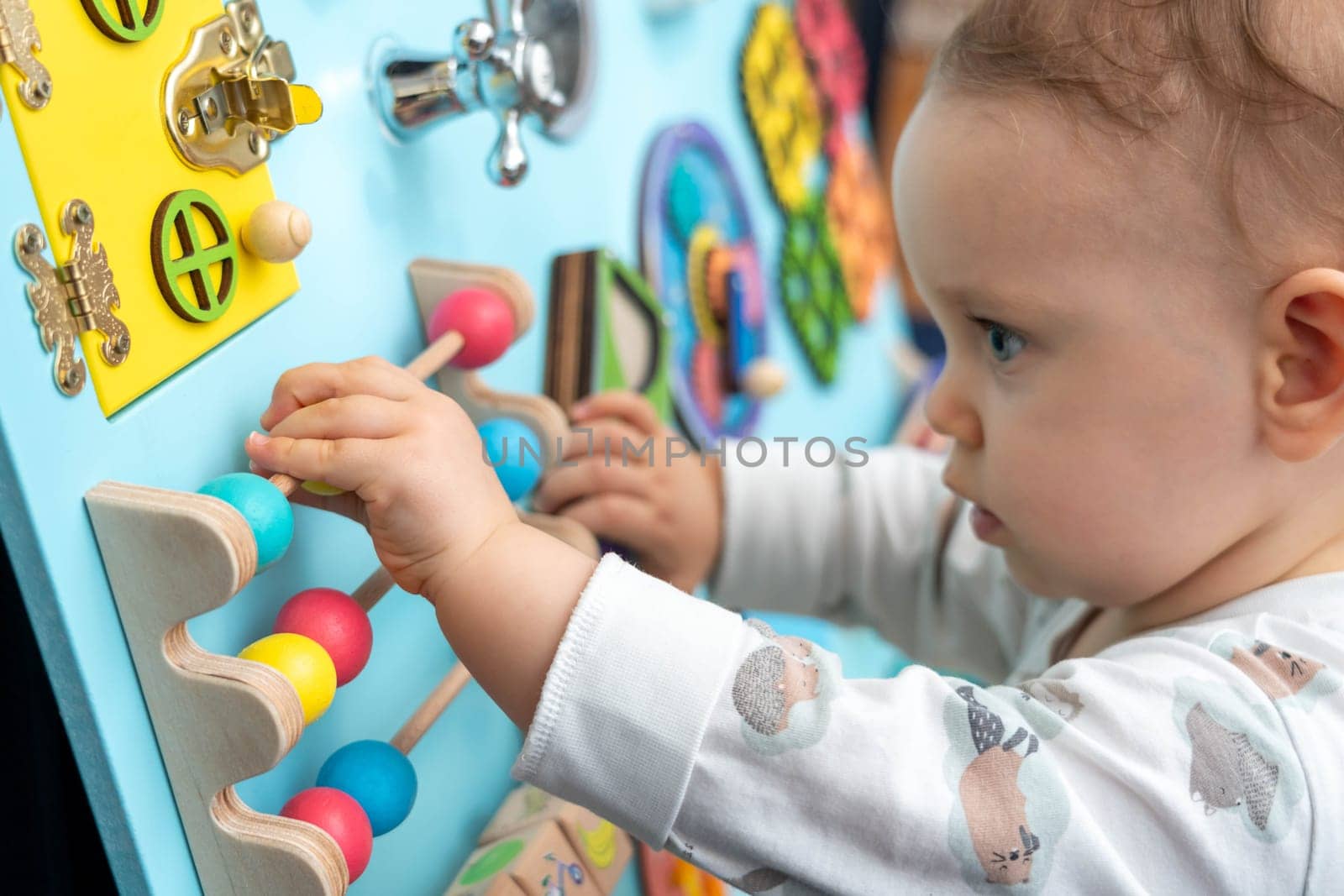 A baby moves round colored wooden elements on a busy board.
