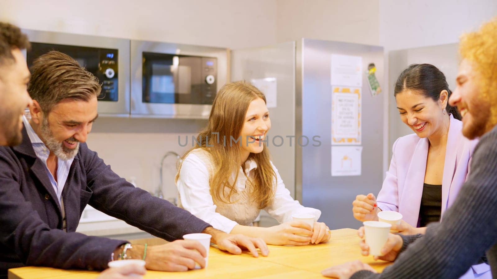 Coworkers laughing while drinking coffee during break in the office