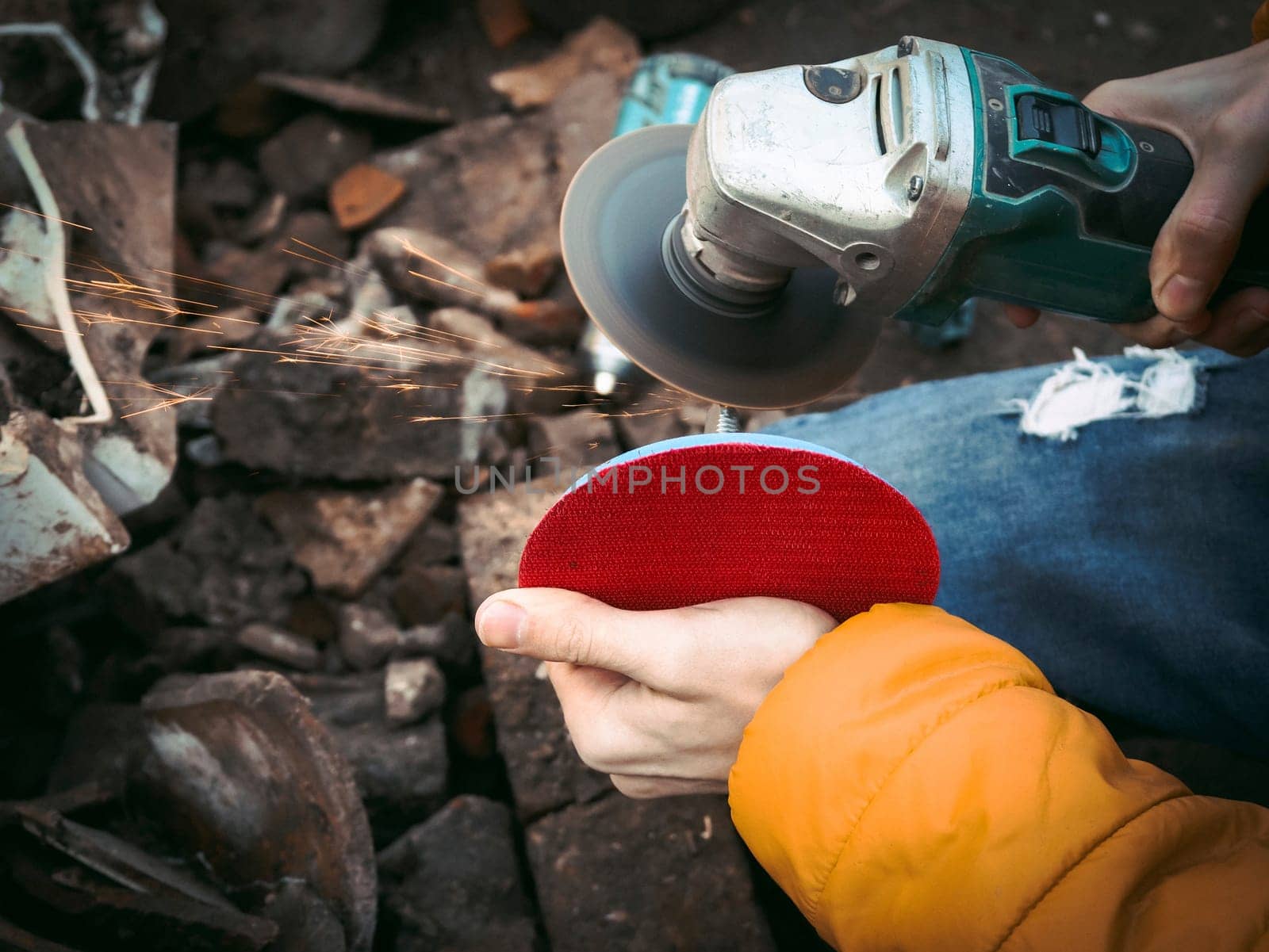The hands of a young caucasian man in a yellow jacket are holding a drill and polishing with a disc by Nataliya