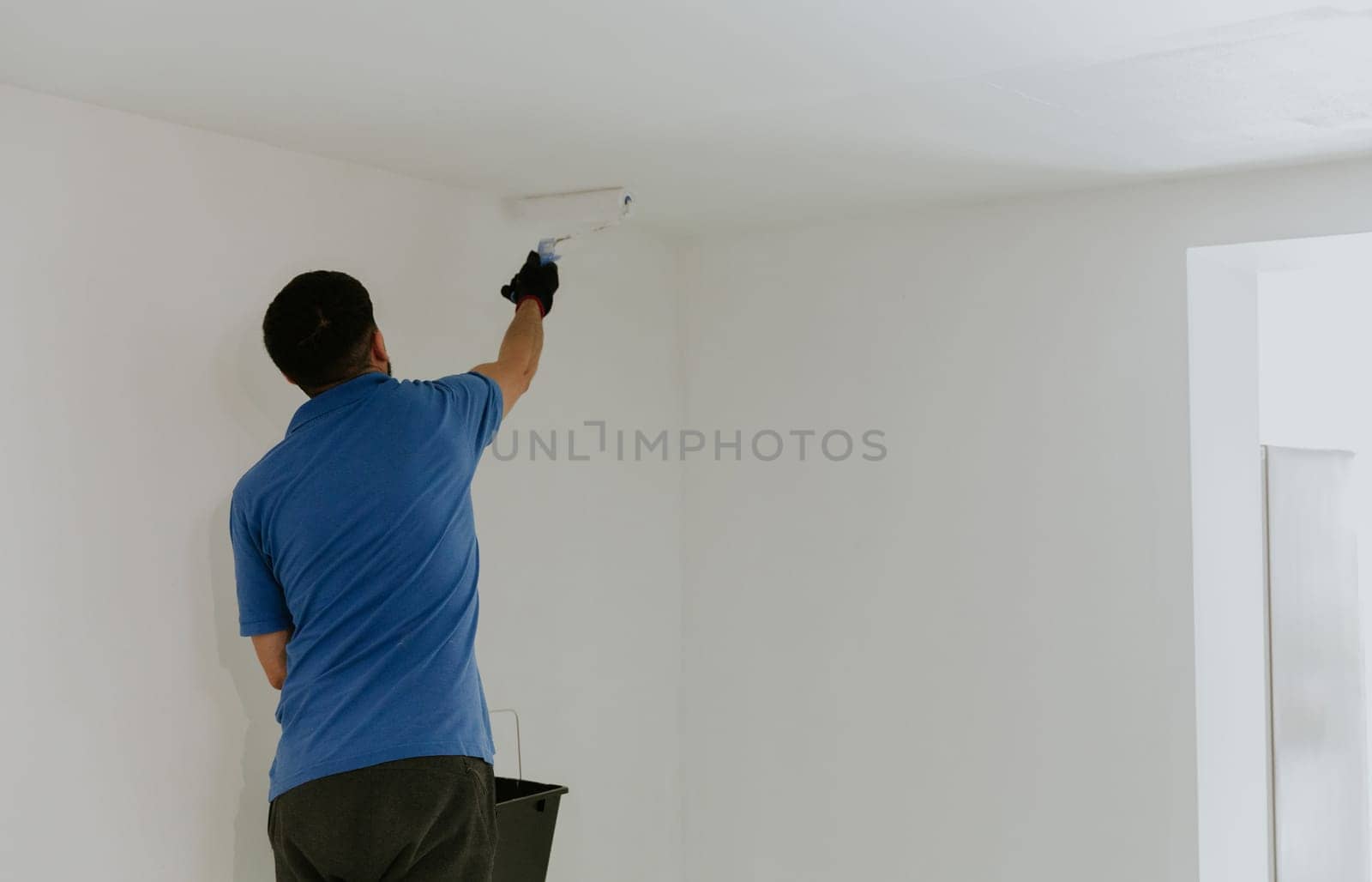 A young oriental man paints the ceiling with a roller. by Nataliya