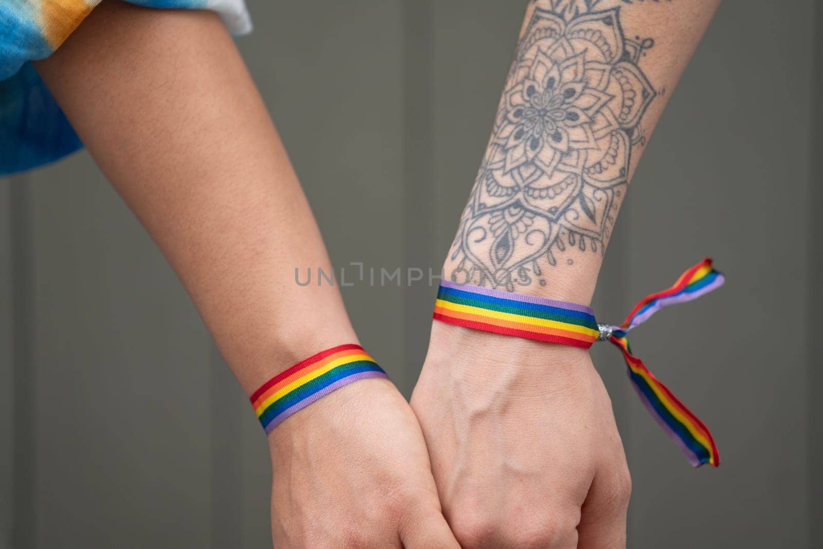 Close up of lesbian couple hands holding together showing love with rainbow bracelets.