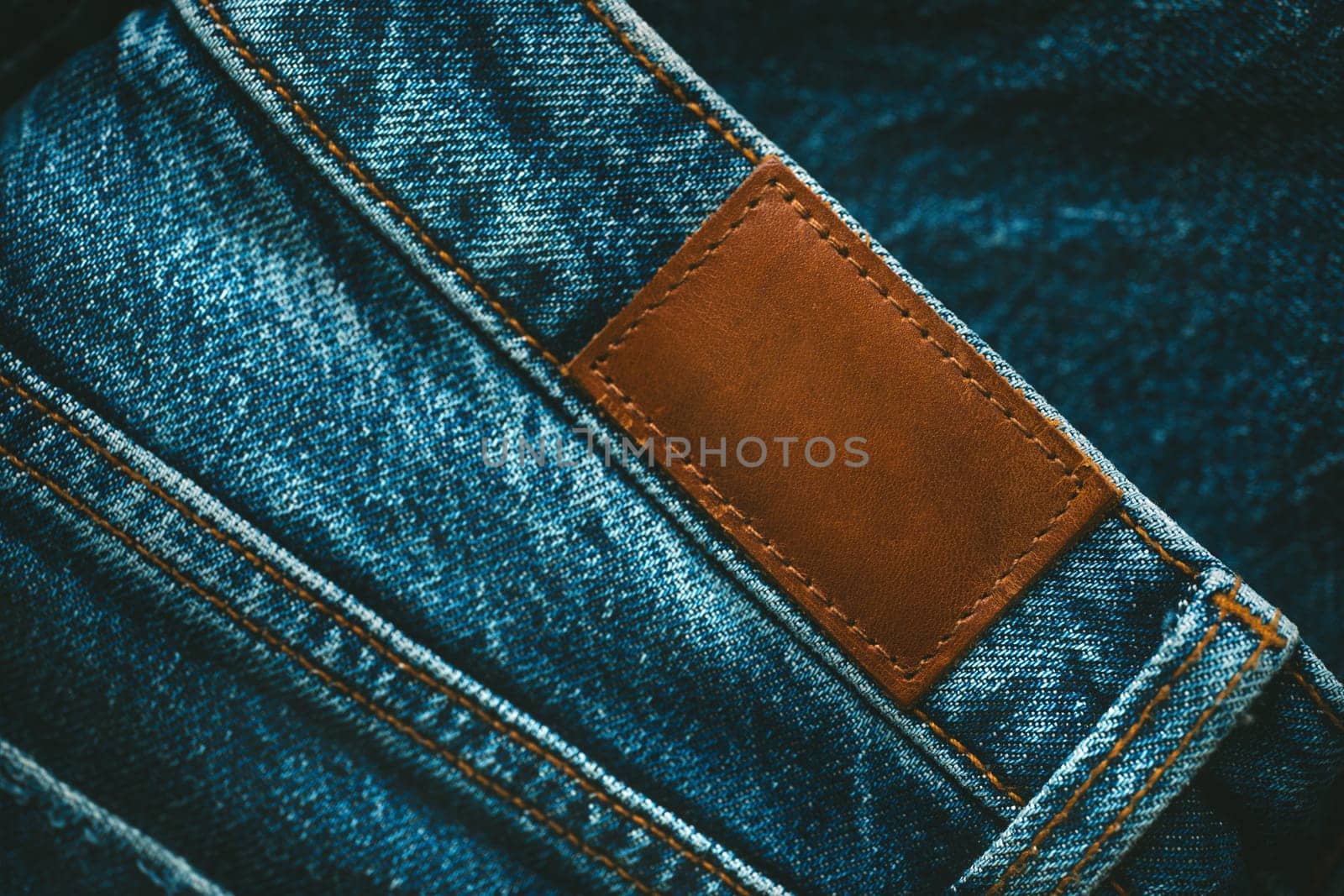Blank brown leather empty jeans label sewed on a blue jeans denim. Style, denim and store concept. by DariaKulkova