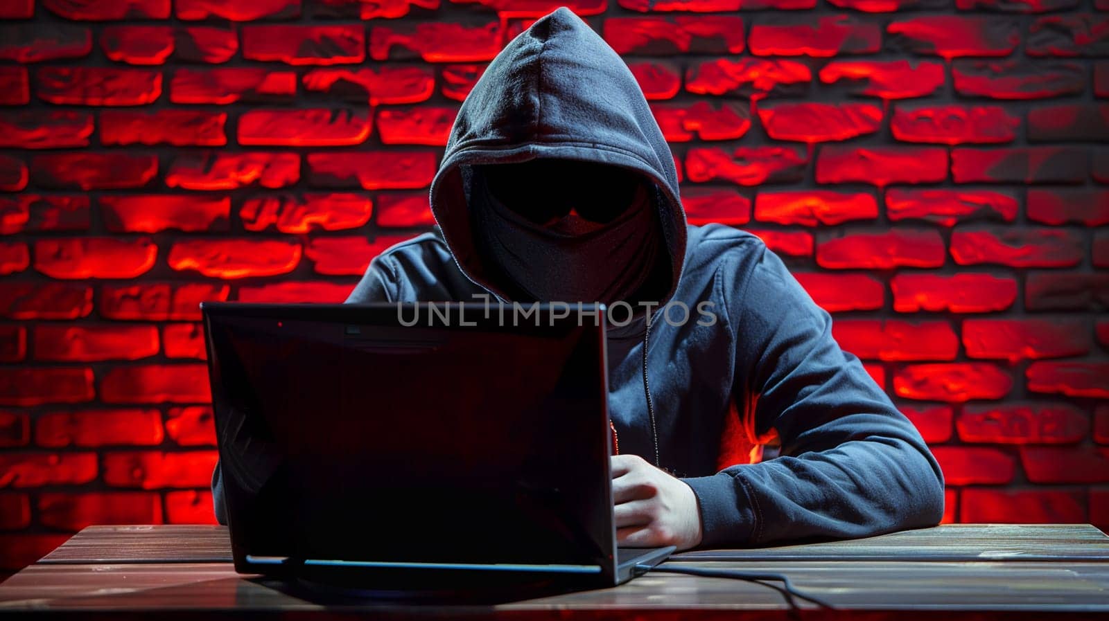 Hooded figure engages in cyber activities using laptop, seated against glowing red brick wall backdrop.