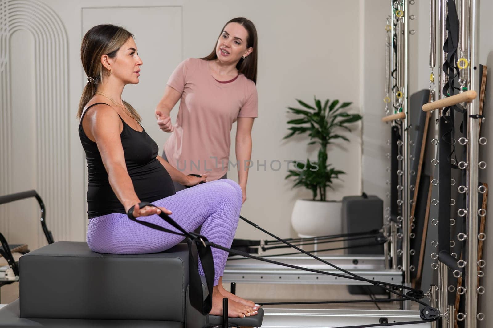 Caucasian pregnant woman doing Pilates exercises on a reformer machine with an individual trainer. by mrwed54