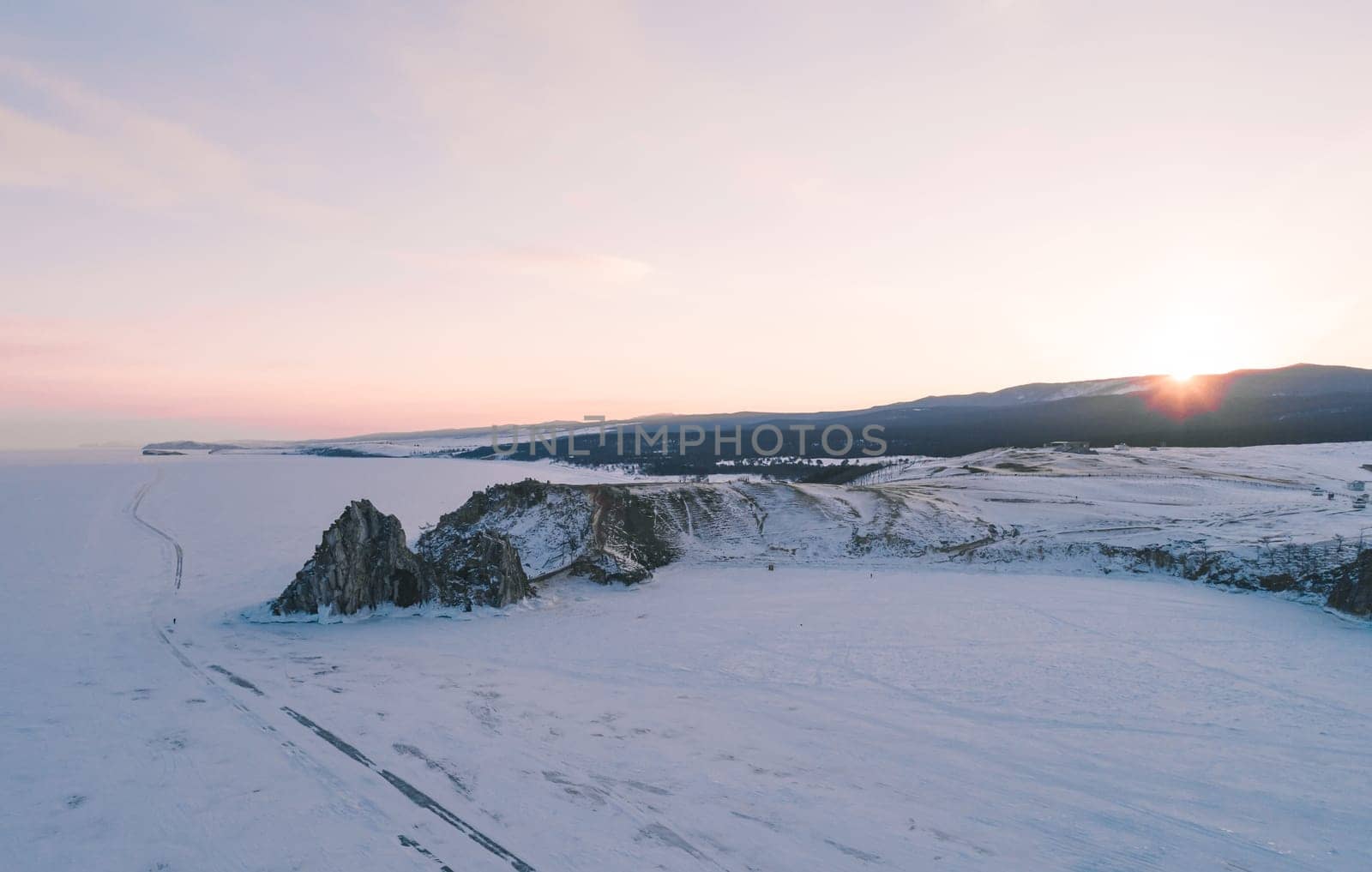 Aerial photo of Shamanka rock and Cape Burkhan on Olkhon at sunset. Beautiful view on frozen Baikal. Panoramic winter landscape