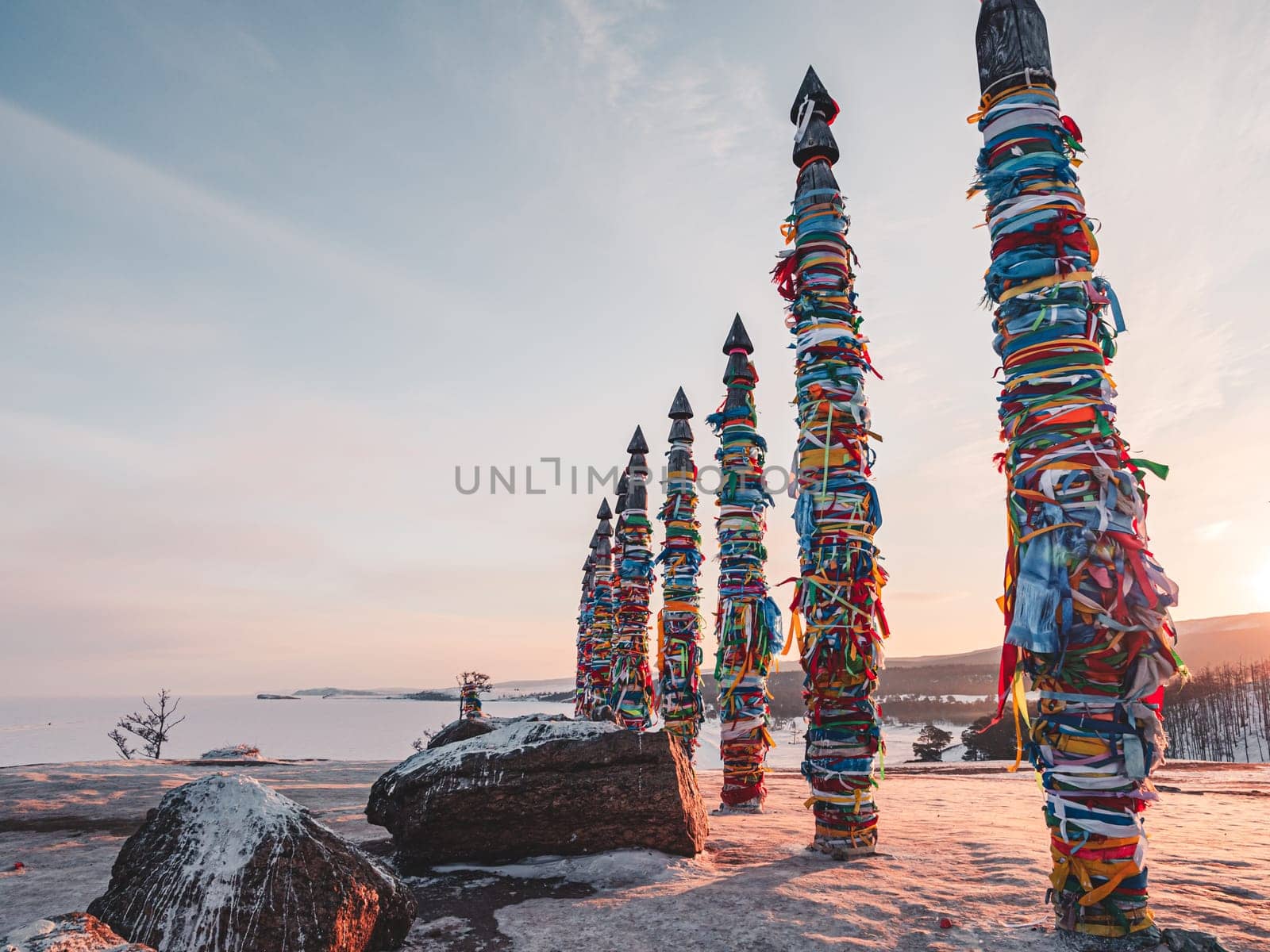 Traditional buryat shaman sacred pillars with colorful ribbons in winter at sunset, cape Burkhan, Olkhon island. Winter Baikal.