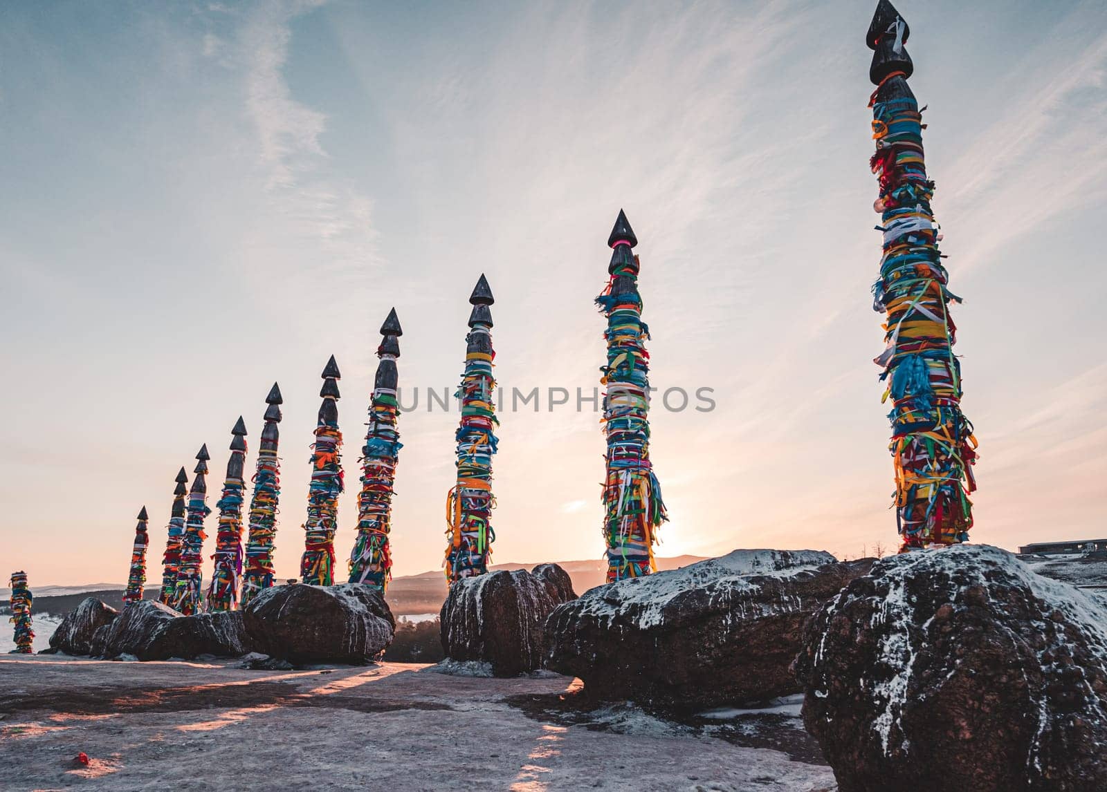 Traditional buryat shaman sacred pillars with colorful ribbons in winter at sunset, cape Burkhan, Olkhon island. Winter Baikal.