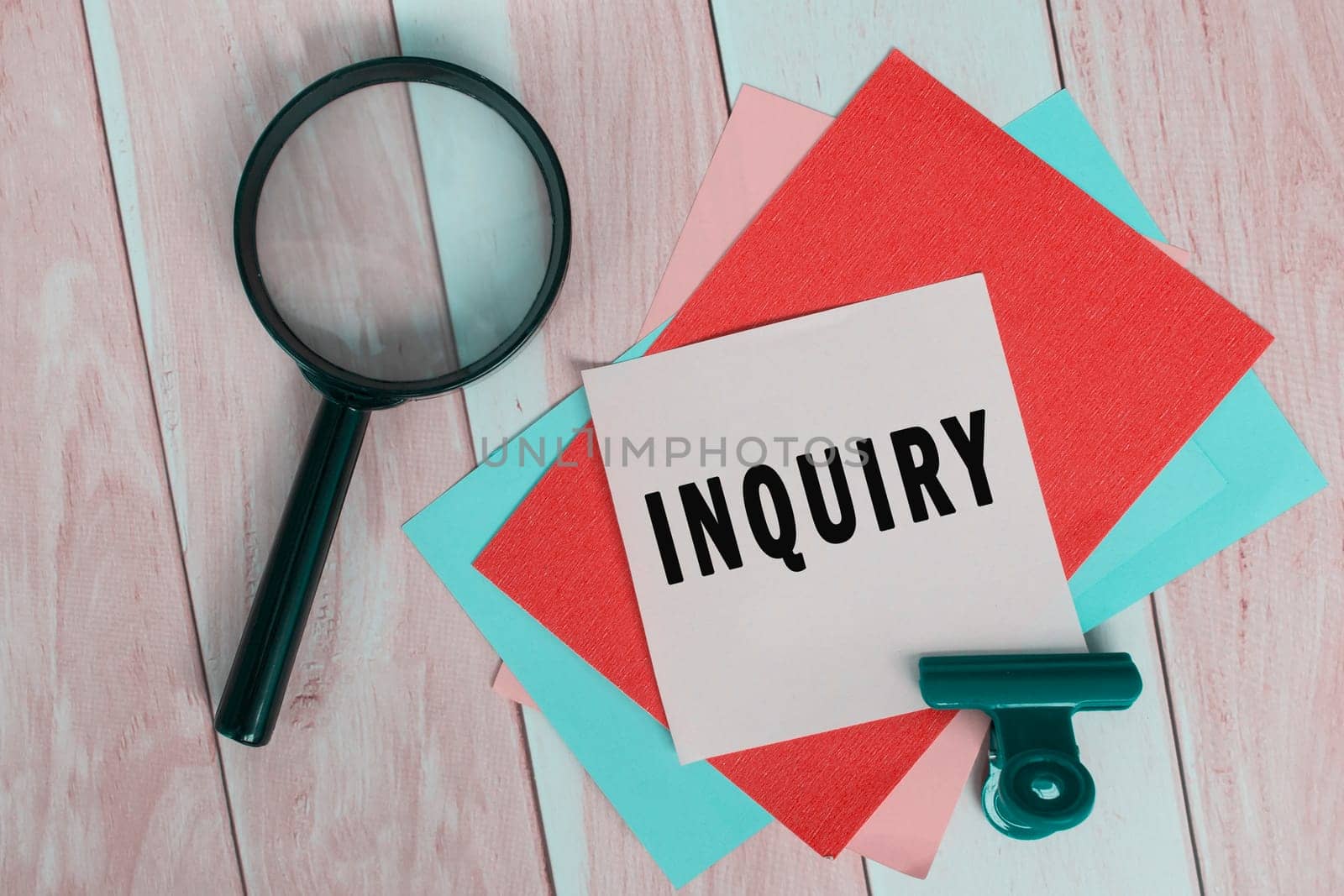 Inquiry word on colorful adhesive paper with magnifying glass on wooden desk.