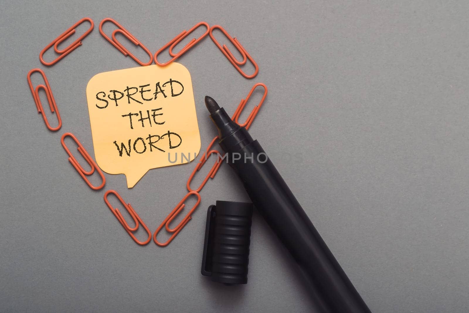 A black pen with a yellow note that says Spread the word. The note is surrounded by paper clips, creating a heart shape