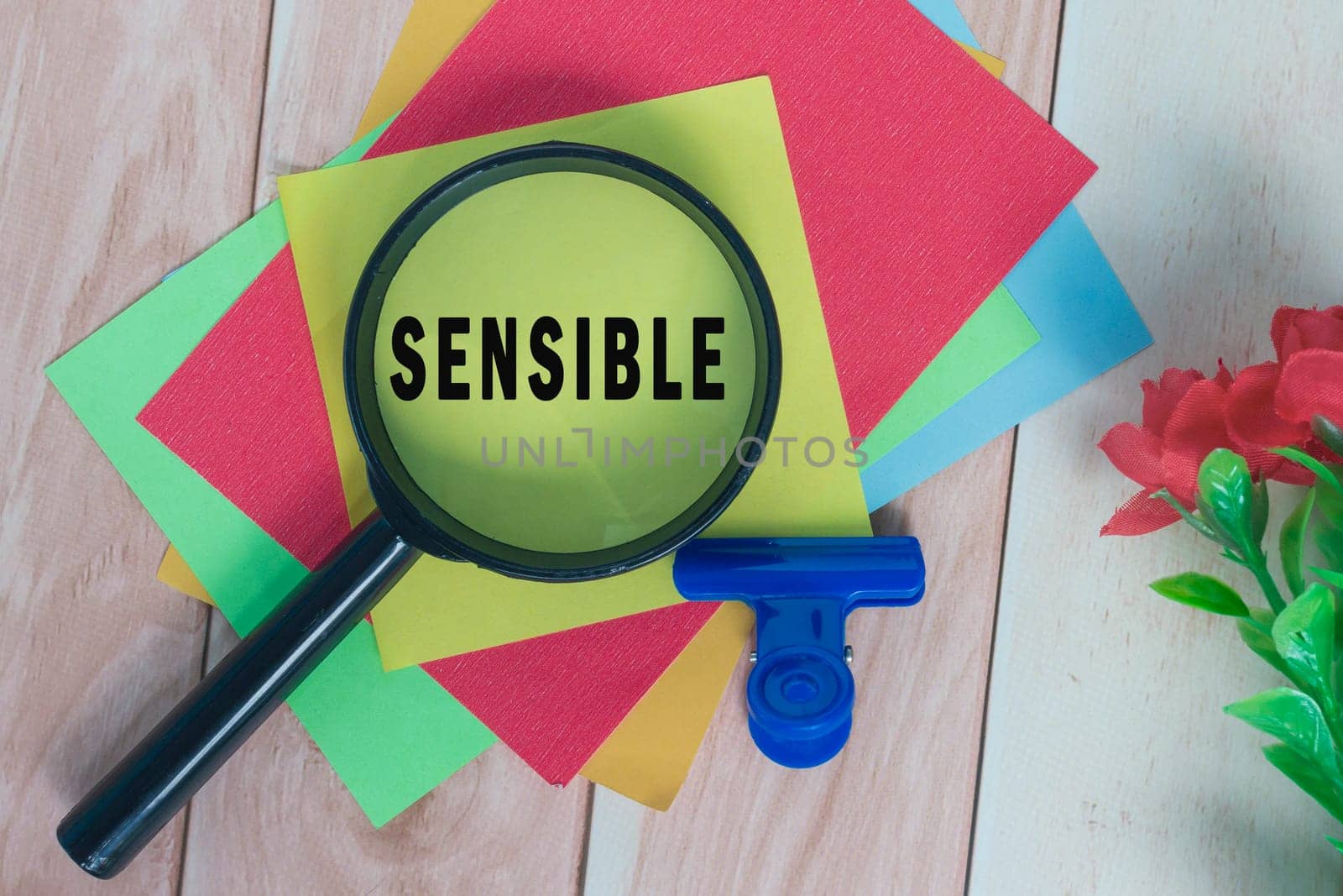Sensible word on colorful adhesive paper with magnifying glass on wooden desk.