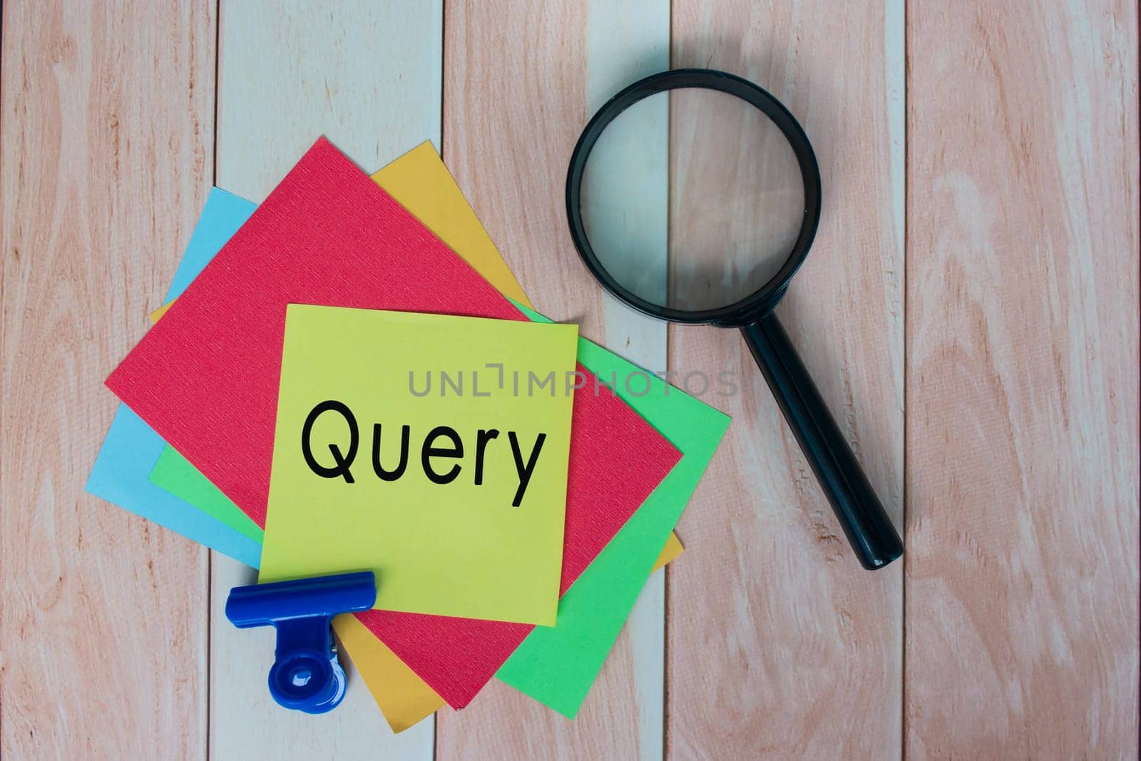 Query word on colorful adhesive paper with magnifying glass on wooden desk.