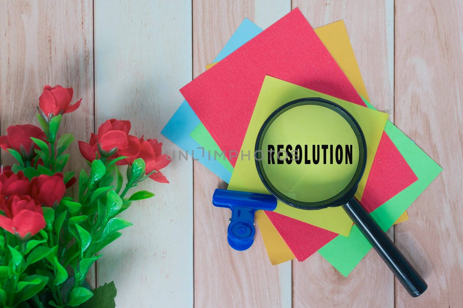 Resolution word on colorful adhesive paper with magnifying glass on wooden desk. by JennMiranda