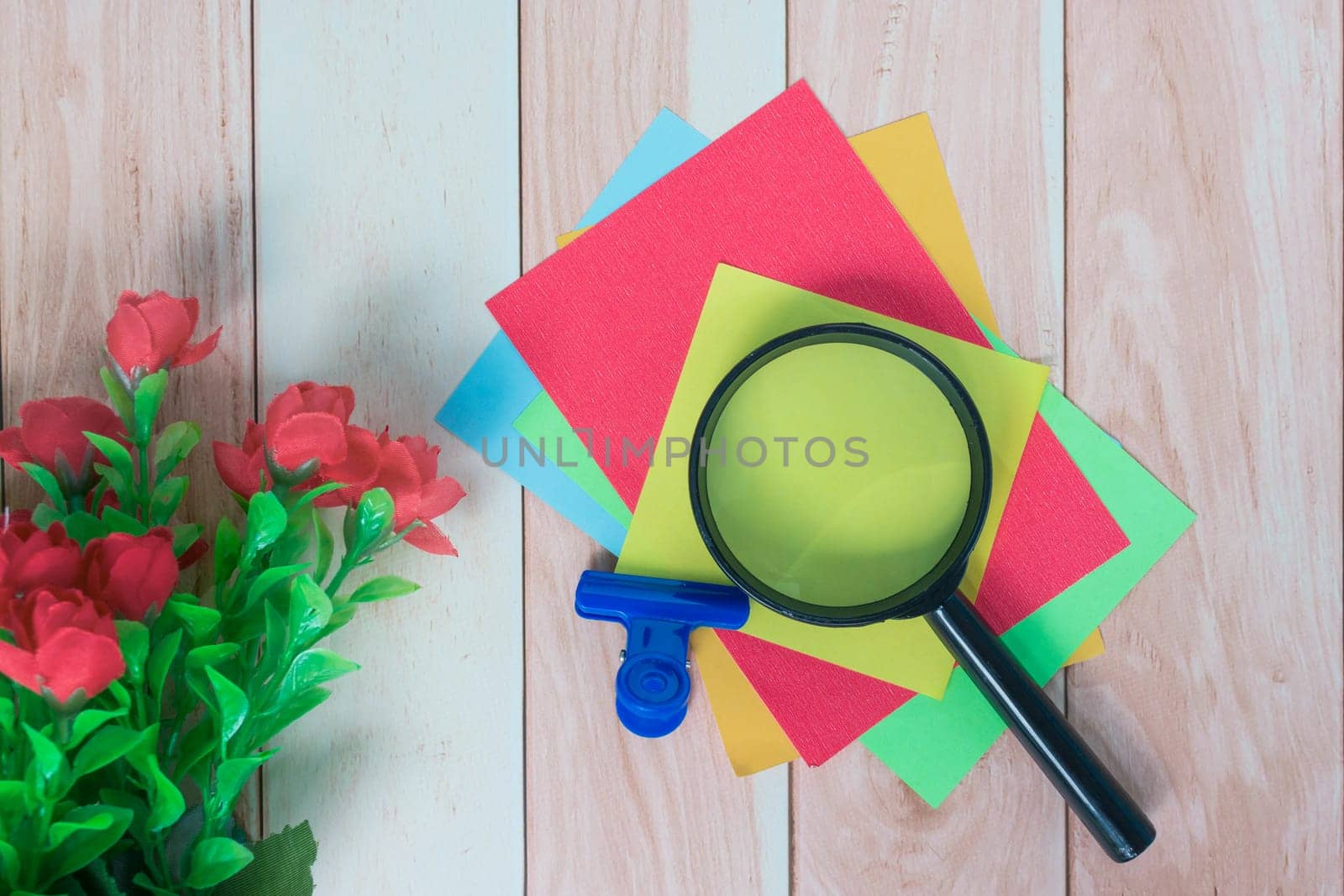 Colorful adhesive paper with magnifying glass on wooden desk. by JennMiranda