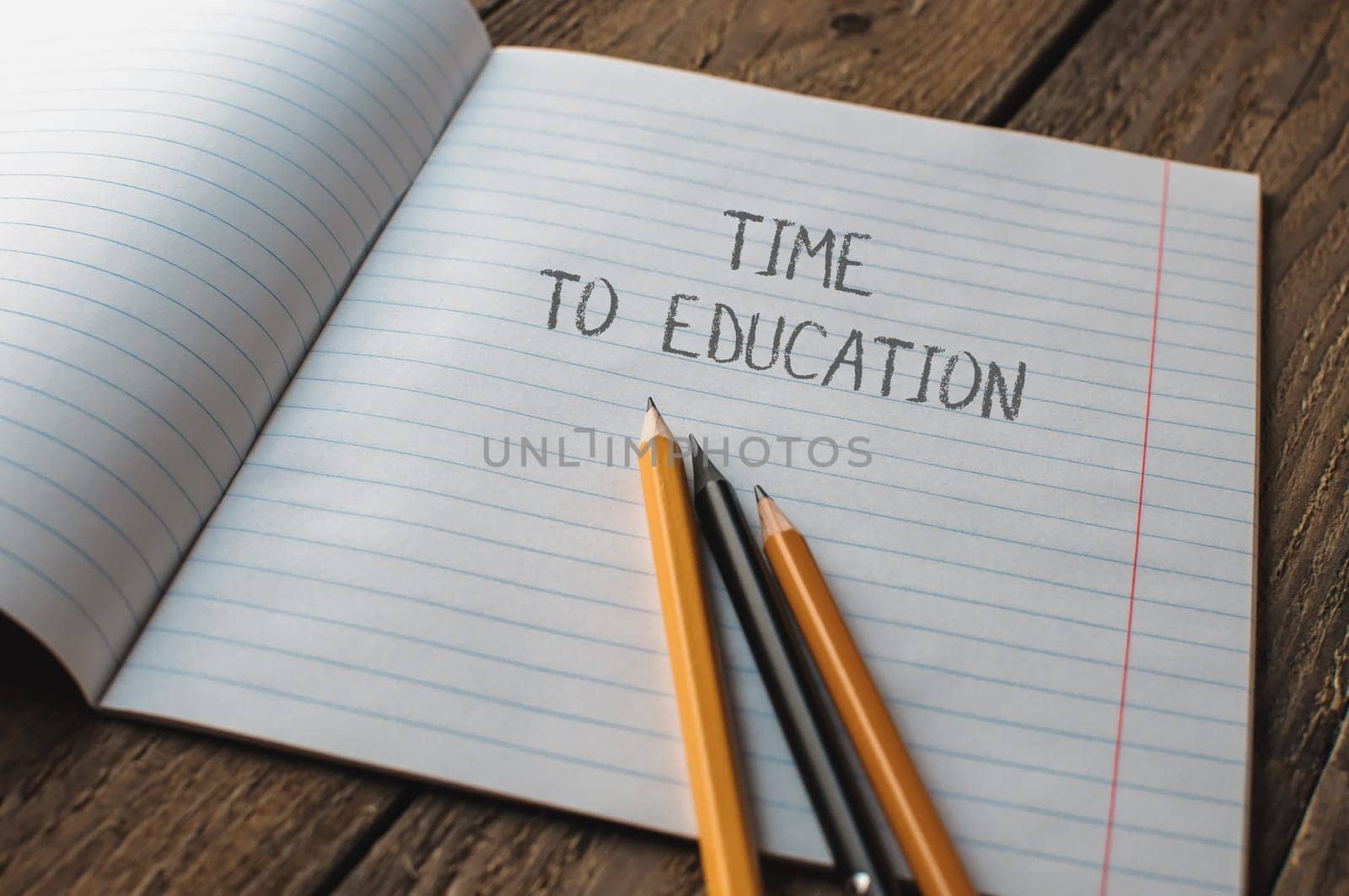 A notebook with pencils on it and the words time to education written on it. The pencils are placed on the paper in a way that they look like they are ready to be used for writing