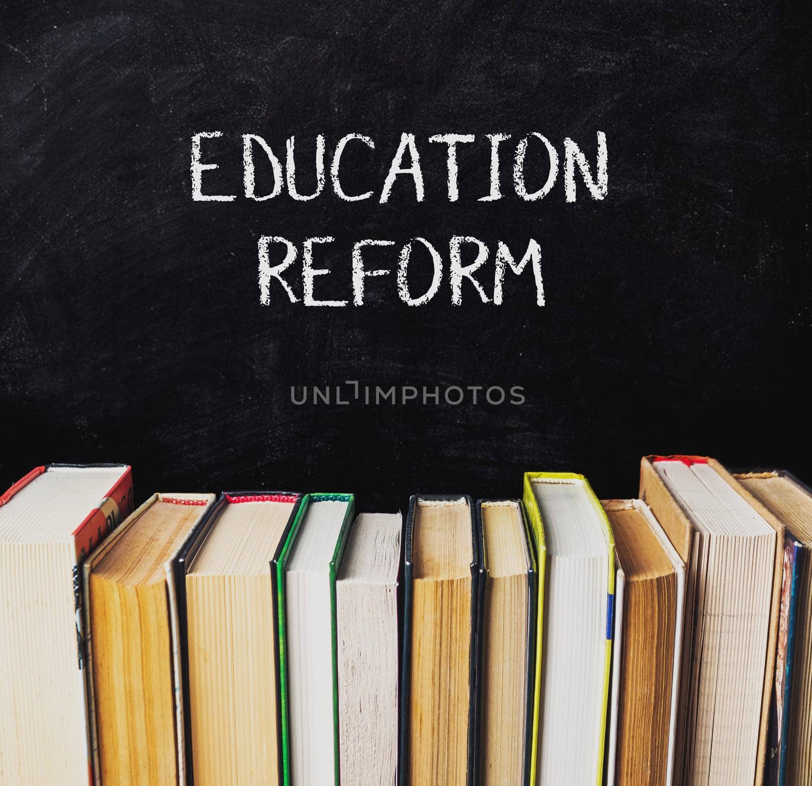 A chalkboard with the words Education Reform written on it. The chalkboard is covered with books, some of which are open