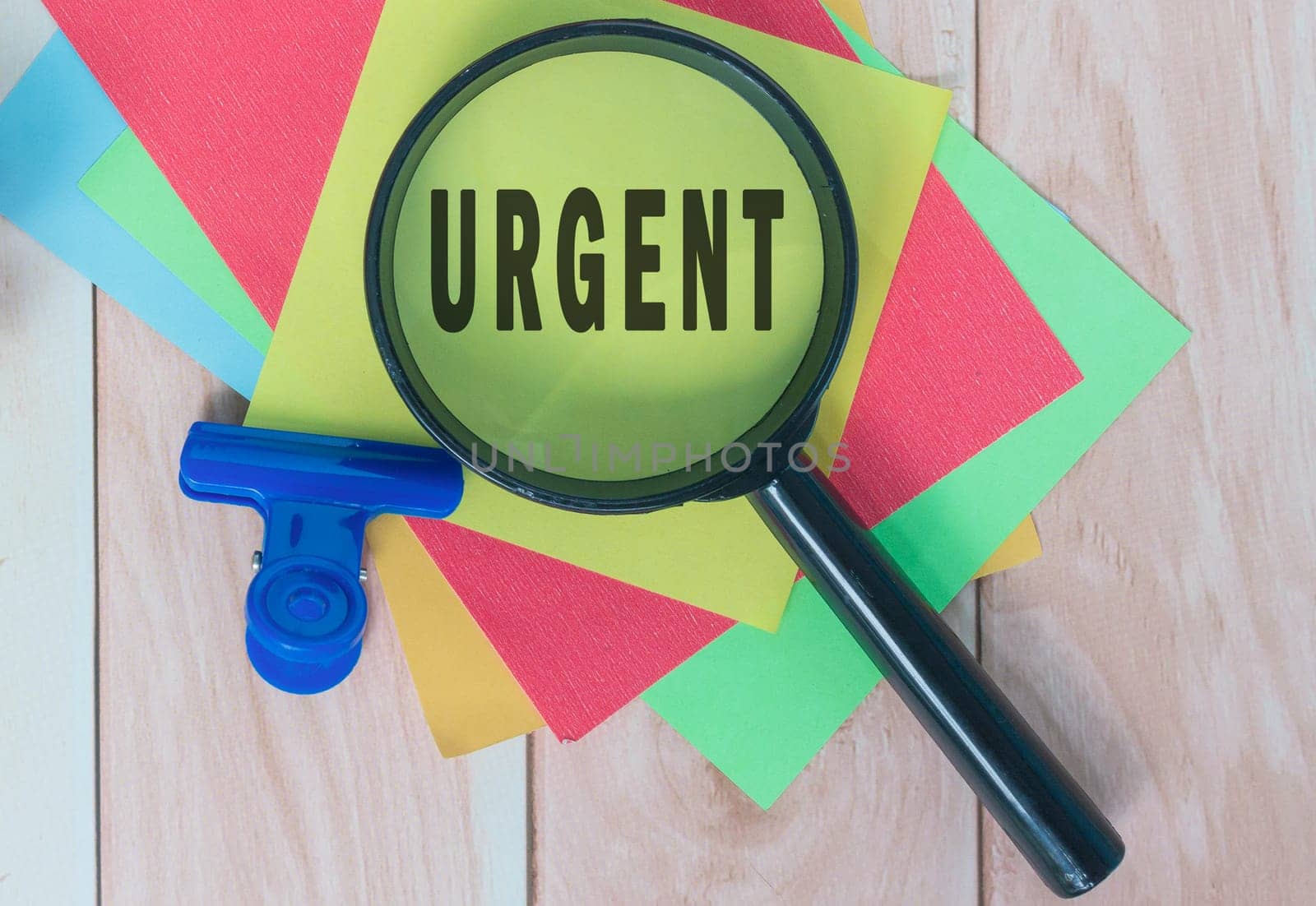 Urgent word on colorful adhesive paper with magnifying glass on wooden desk.