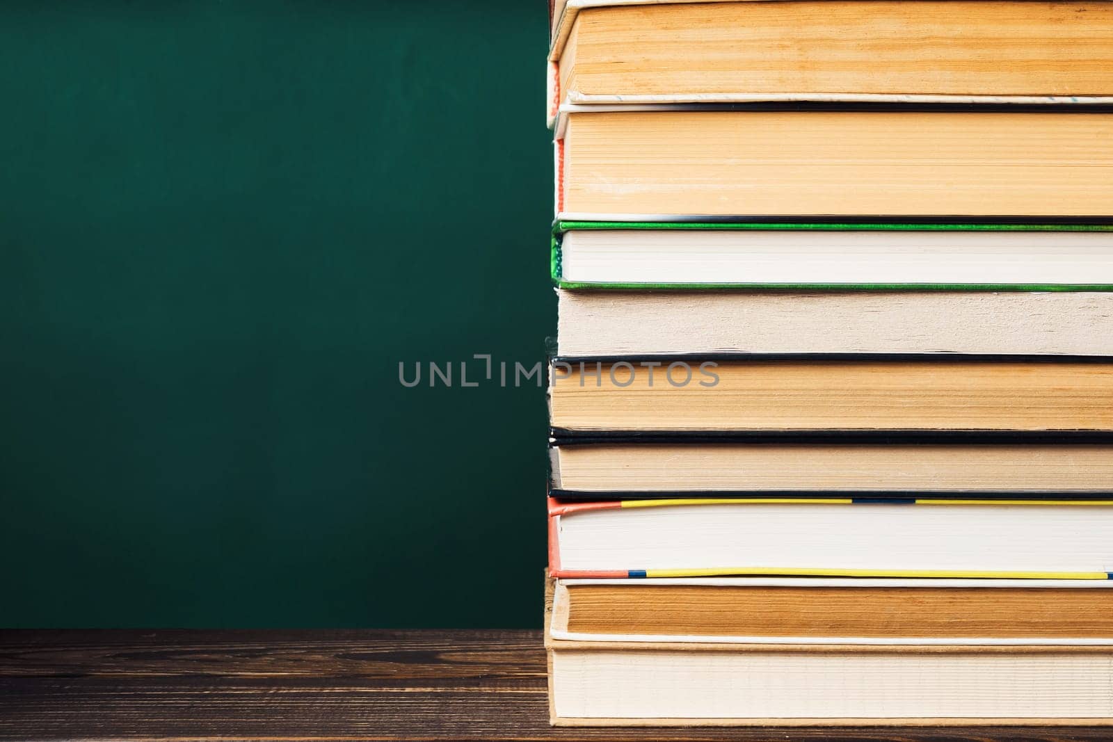 A stack of books on a table with a green background. The books are of different sizes and colors. Concept of knowledge and learning, as well as the importance of reading and education