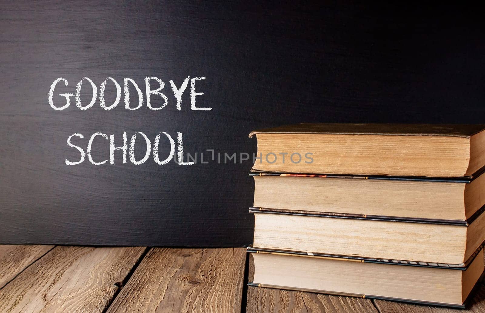 A stack of books with the word Goodbye School written on a chalkboard. The books are piled on top of each other, creating a sense of nostalgia and longing for the past