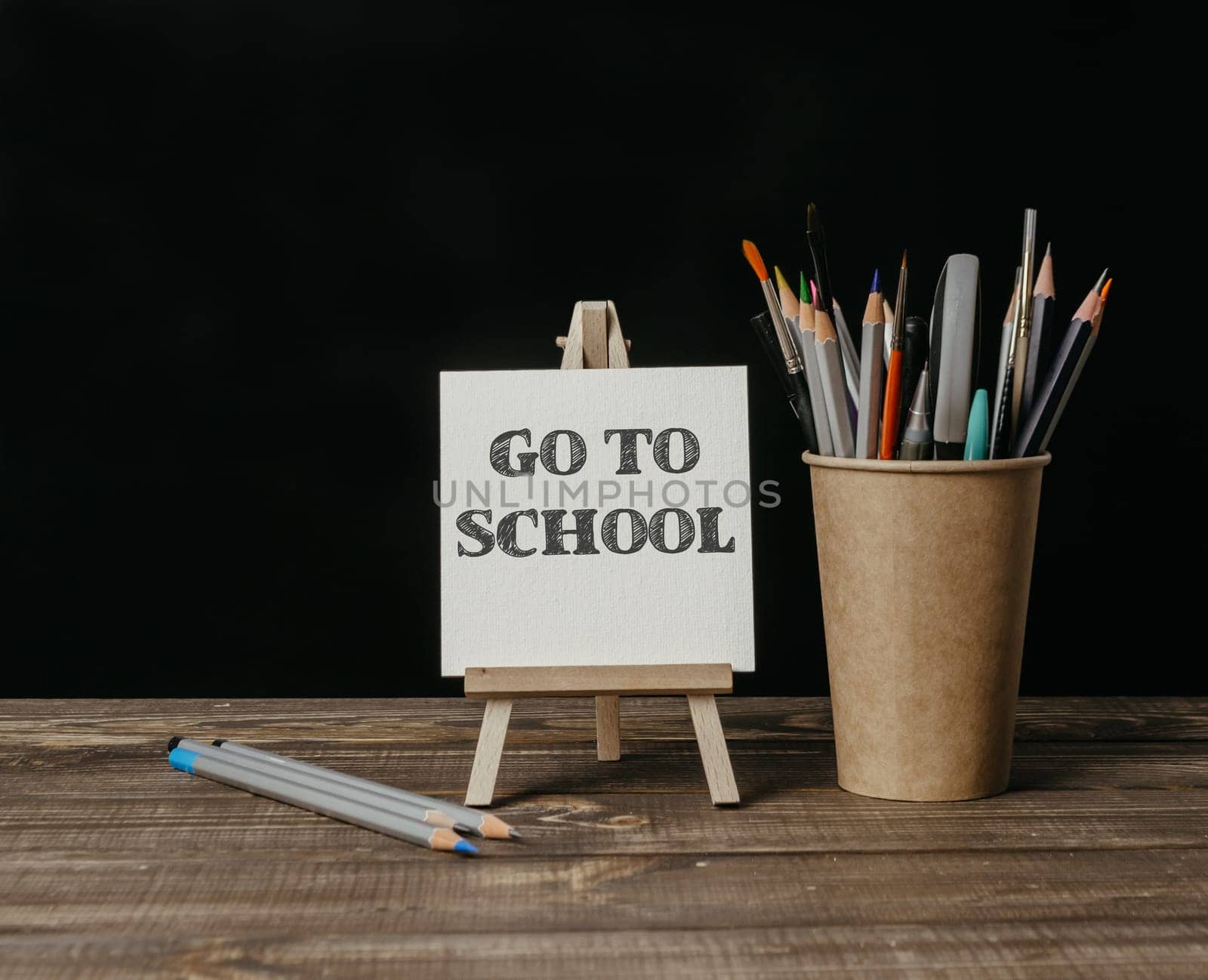 A wooden desk with a white sign that says Go to School and a cup of pencils. High quality photo