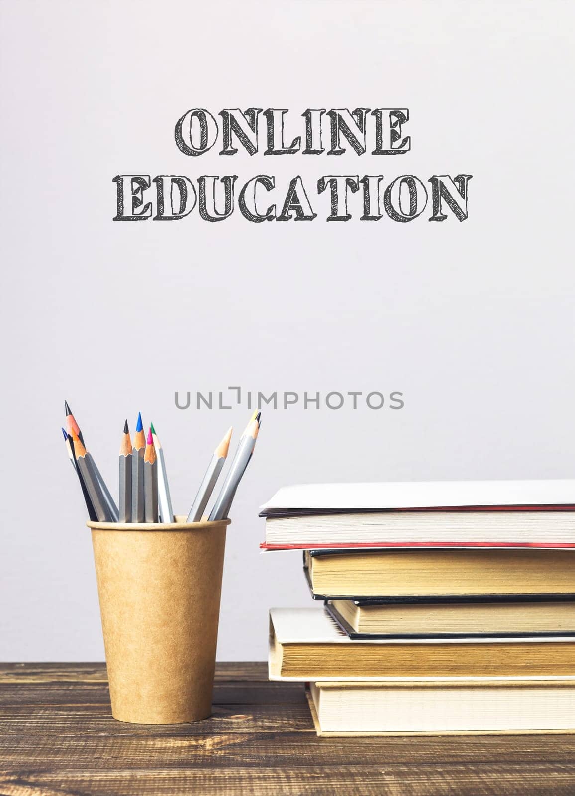 A stack of books and a pencil holder on a table with the words online education written above them