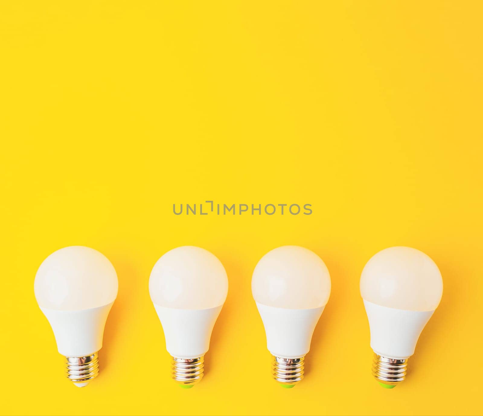Four white light bulbs are arranged on a yellow background. The bulbs are all the same size and shape, and they are evenly spaced out. Concept of uniformity and order, as the bulbs are all identical