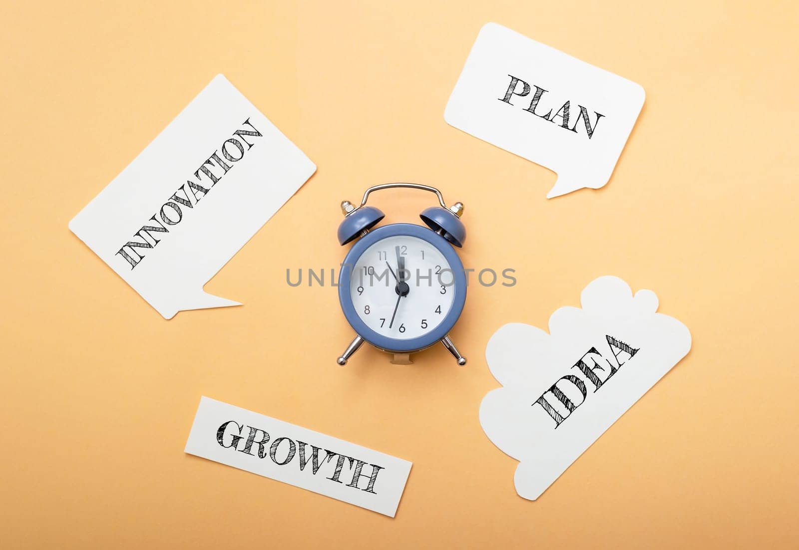 A clock sits on a table with a bunch of paper with words like growth, plan, innovation, idea and growth written on them