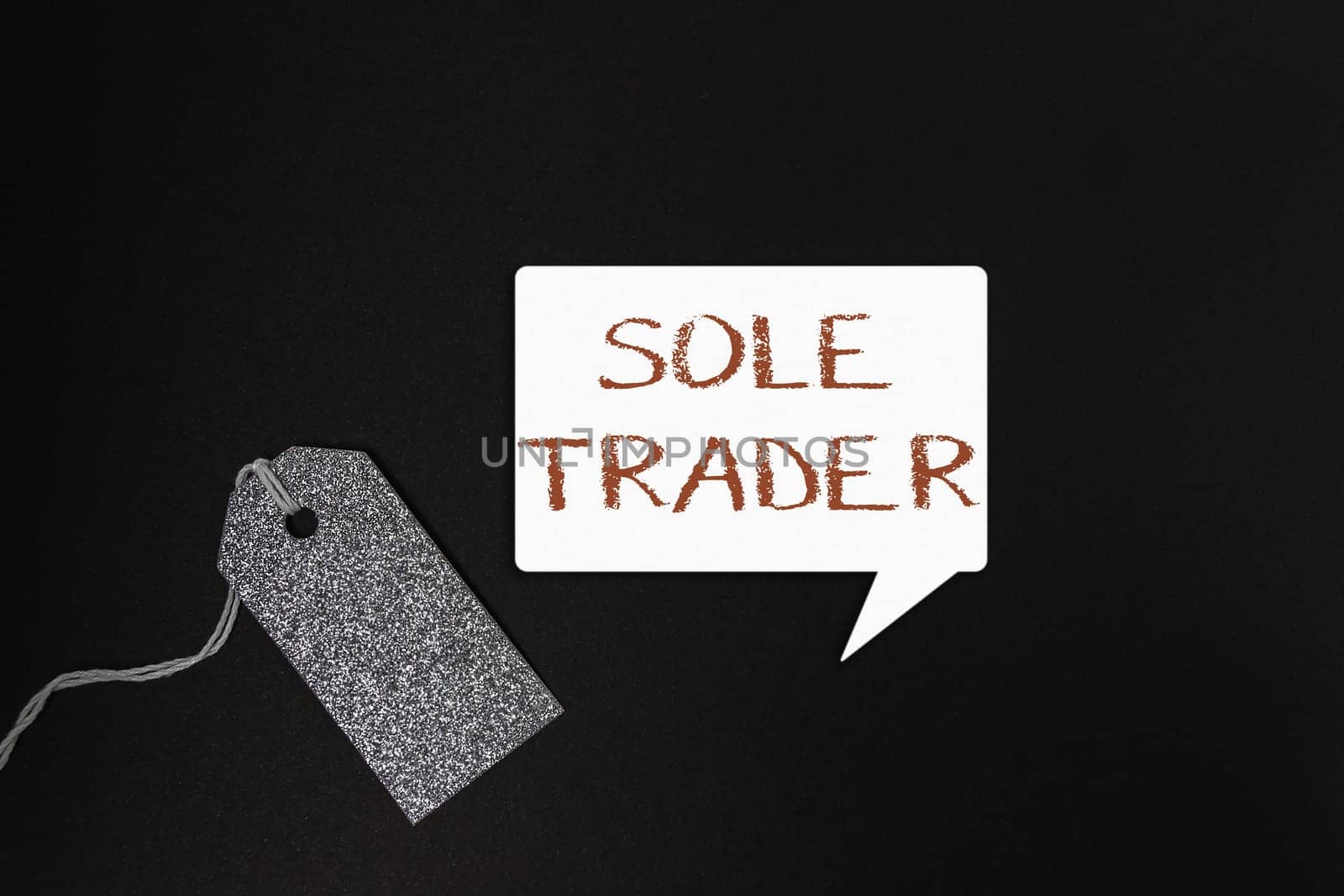 A tag with the word Sole Trader written on it. The tag is hanging from a chain. The image is black and white