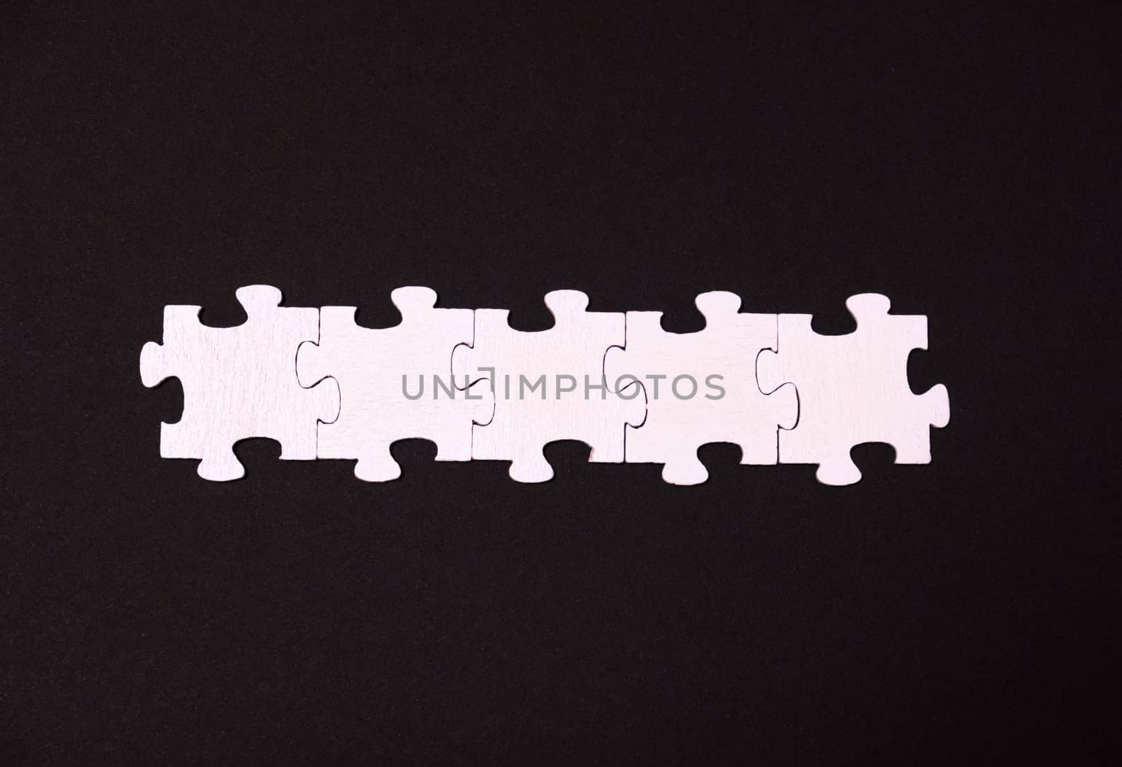 A row of white puzzle pieces on a black background. Concept of order and structure, as the pieces are neatly arranged in a row. The black background adds a sense of contrast and focus to the image