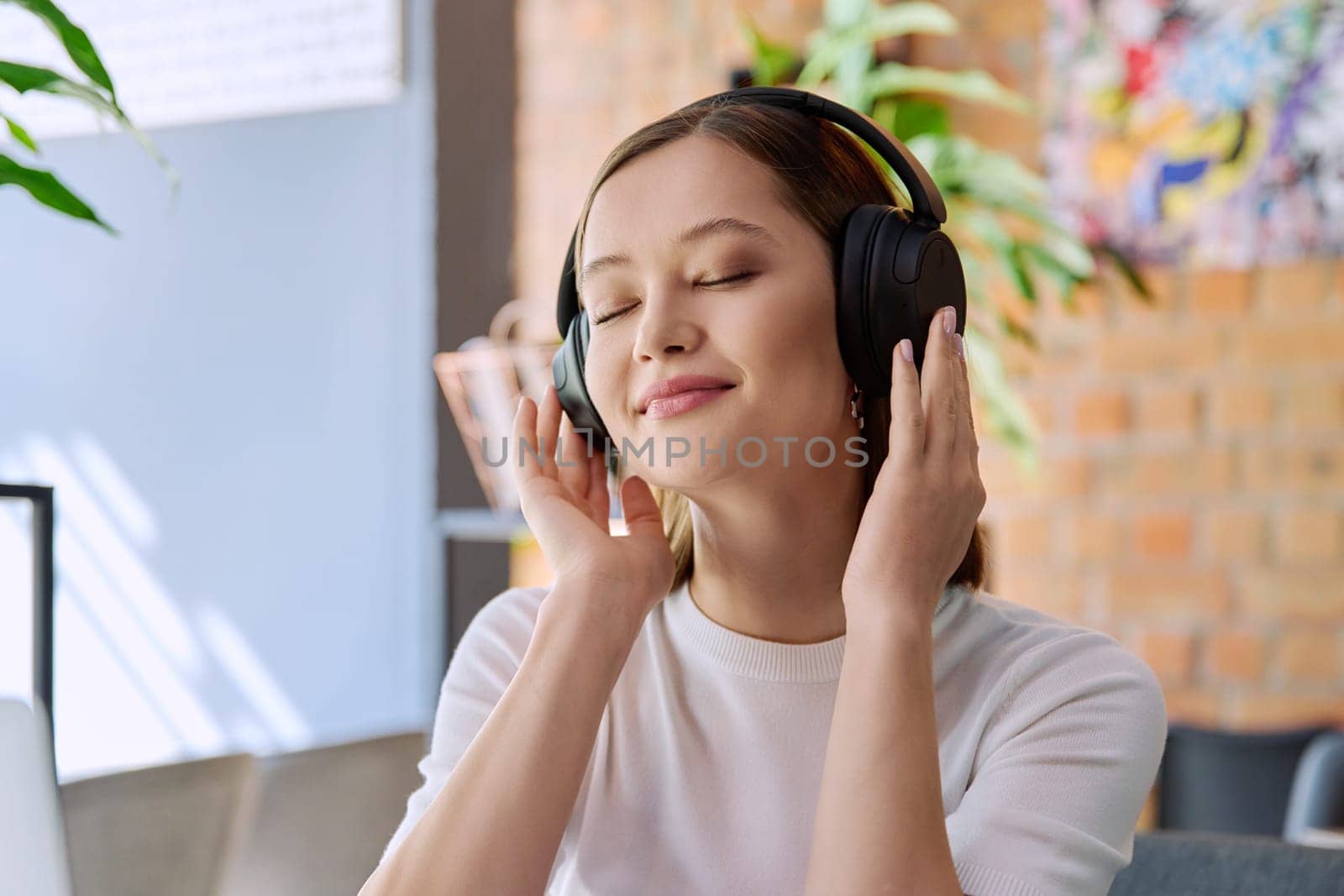 Young happy woman in headphones with closed eyes enjoying music, audio text book. Technology, lifestyle, youth concept