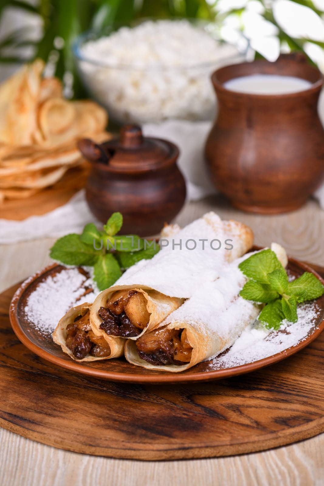 Homemade thin pancakes. The apples are cooked in a buttery caramel sauce with raisins and cinnamon and stuffed into a thin pancake. Garnish with powdered sugar and mint. Food in a rustic style.