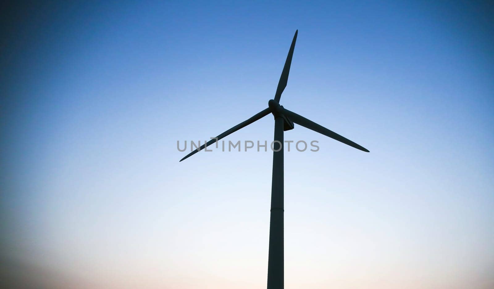 Wind turbine silhouette against a blue sky. View from the bottom point. by Hil