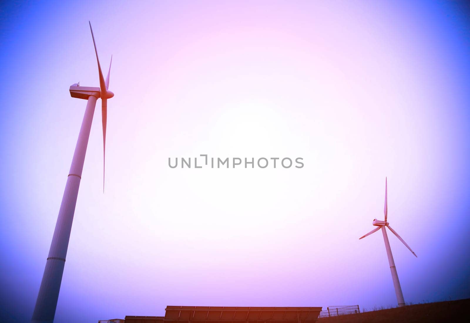 A cluster of wind turbines stand tall against a clear blue sky, their blades spinning energetically to harness wind power for energy generation.