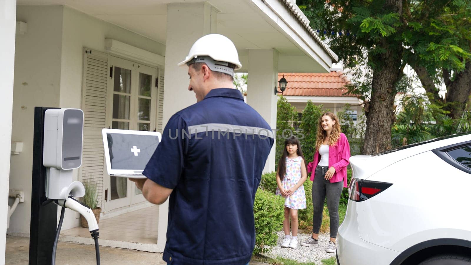 Qualified technician working on home EV charging station installation, making troubleshooting and configuration setup on charging system with empty laptop screem for EV at home. Synchronos