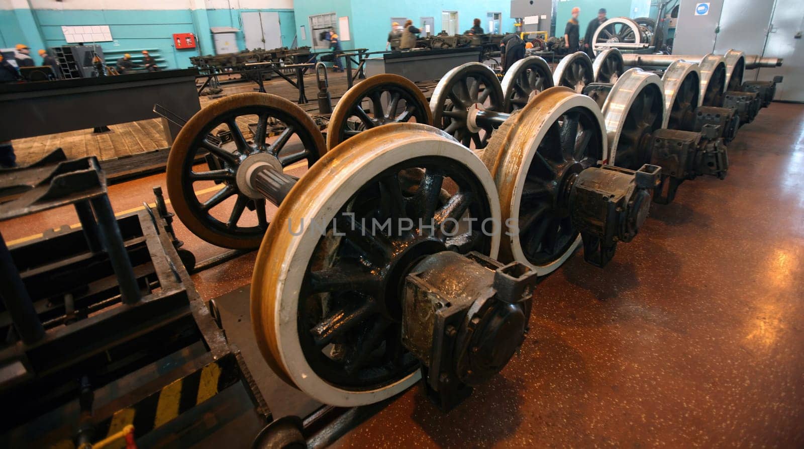 The workshop showcases the maintenance of railway equipment with a focus on a locomotive and a set of gleaming train wheels. Workers are possibly present, tending to the overhaul and repair of these vital components that keep the transportation network running smoothly. The setting suggests routine upkeep, keeping safety and efficiency at the forefront.