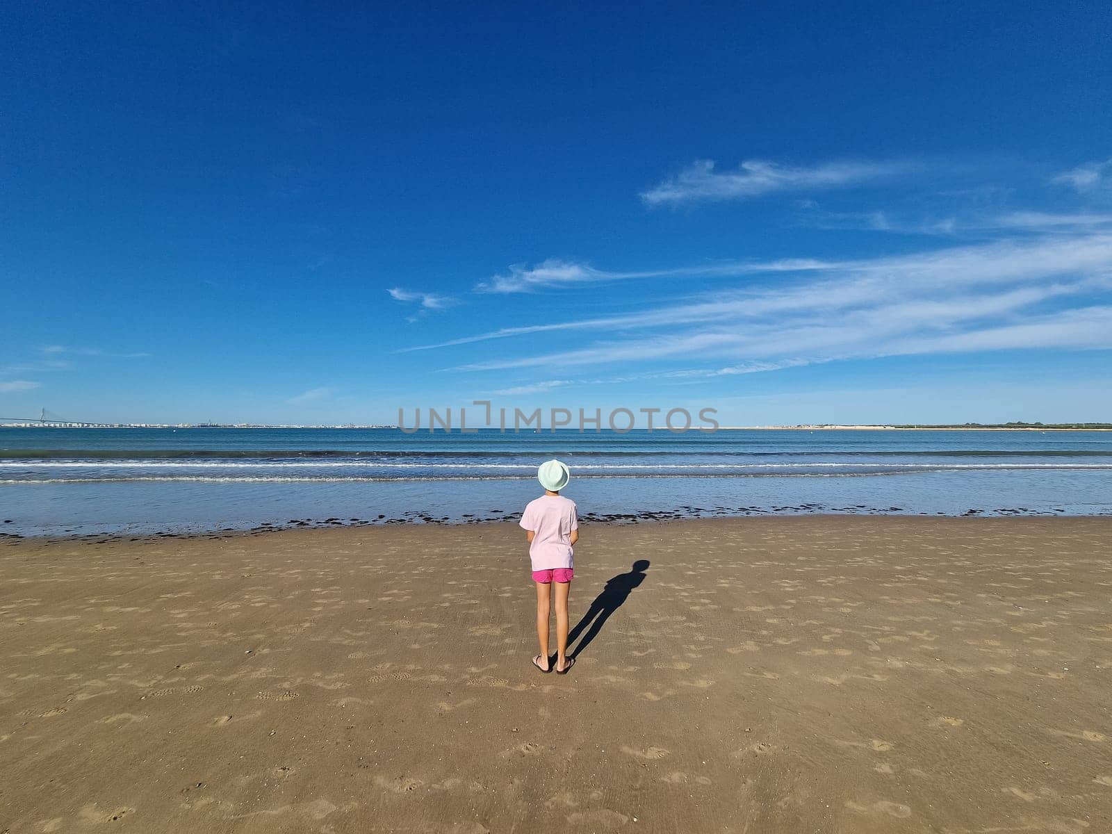 Girl with hat in front of the sea, on a sandy beach. Valdelagrana Beach in Puerto de Santa Maria, Cadiz, Andalusia, Spain