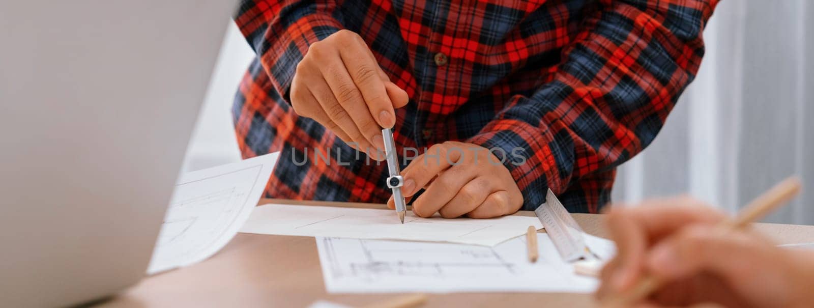 A professional engineer uses divider to measure blueprint during skilled architect drawing blueprint at architectural project meeting. Teamwork and cooperation concept. Closeup. Delineation.