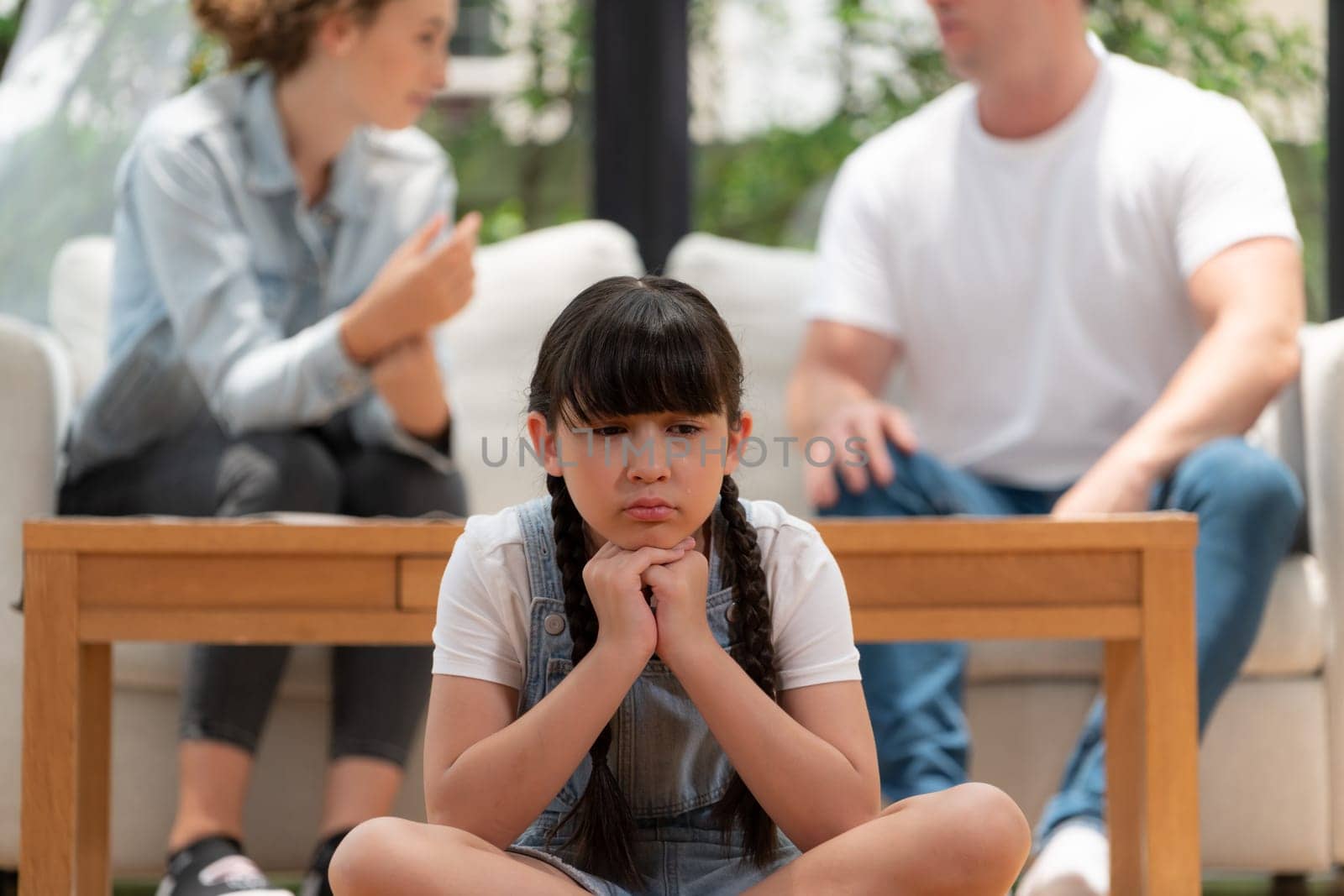 Stressed and unhappy young girl crying and trapped in middle of tension by her parent argument in living room. Unhealthy domestic lifestyle and traumatic childhood develop to depression. Synchronos