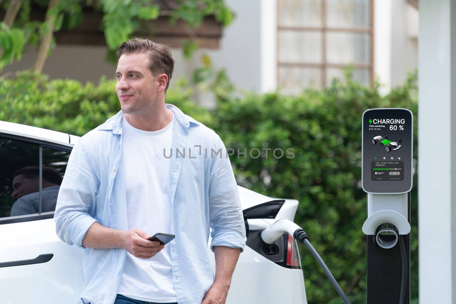 Modern eco-friendly man recharging electric vehicle from home EV charging station. Innovative EV technology utilization for tracking energy usage to optimize battery charging at home. Synchronos