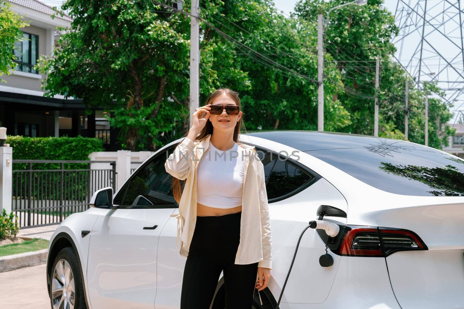 Eco-friendly conscious woman recharging EV vehicle from home charging station. EV electric car technology utilized as alternative transportation for future sustainability. Expedient