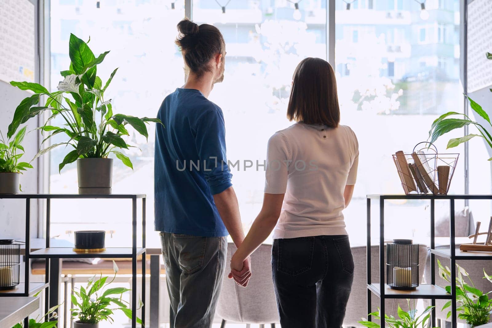 Back view, silhouette of young couple holding hands looking out window. Love friendship romance relationship, happiness, lifestyle, people concept