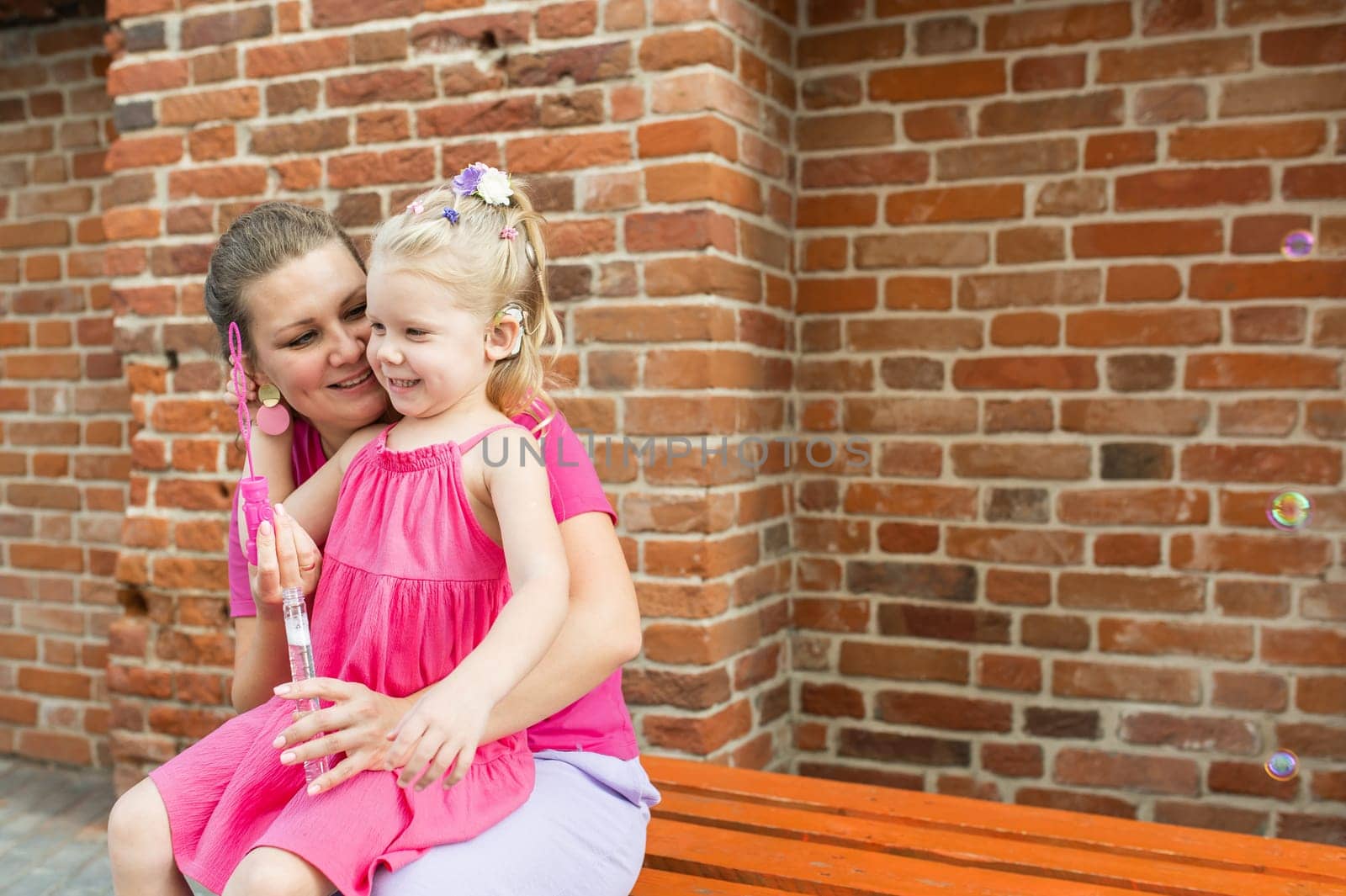 Mother holds and have fun her child with hearing aids and cochlear implants summer outdoor . Deaf and health concept. Diversity and inclusion. Copy space.