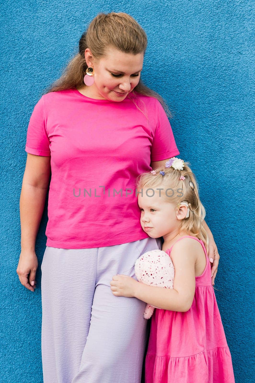 Blonde little girl with cochlear implant playing with her mother outdoor. Hear impairment deaf and health concept. Diversity and inclusion. Copy space.