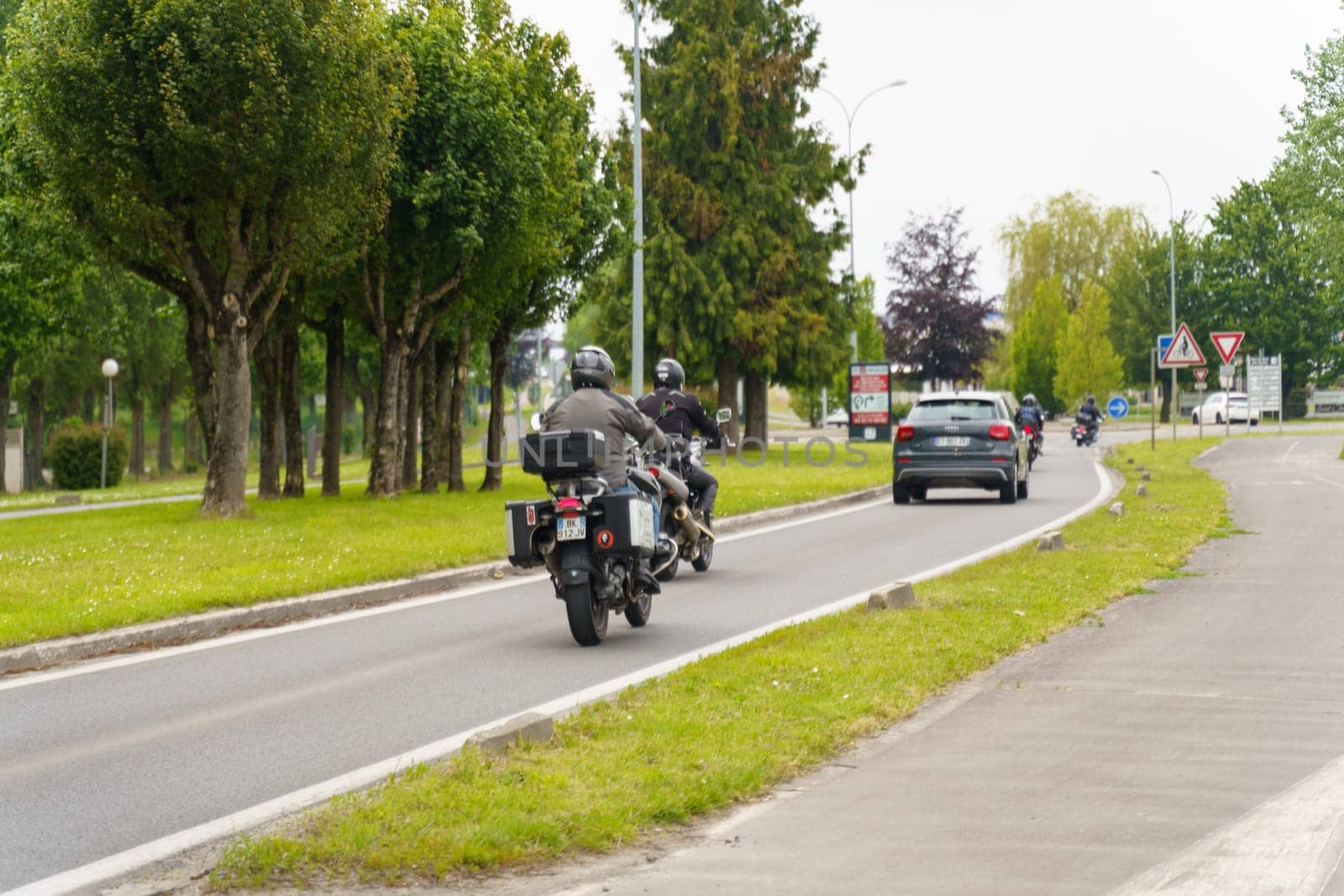 Cambrai, France - May 21, 2023: A group of individuals riding motorcycles down a city street. The riders are moving swiftly, with helmets on, and some are wearing leather jackets.