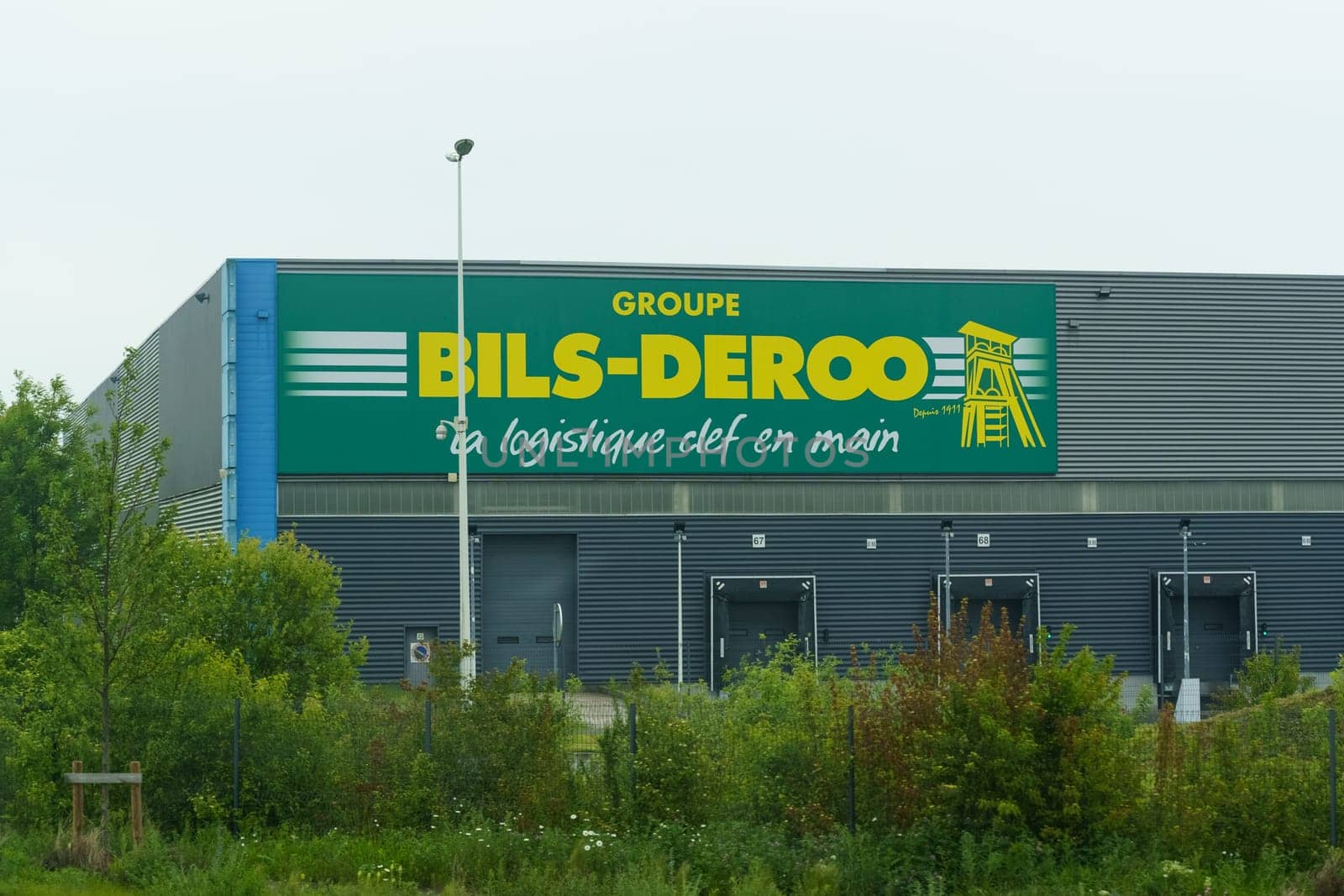 Noyelles-Godeau, France - May 22, 2023: - May 22, 2023:The facade of Bils-Deroos logistics warehouse, showcasing the companys signage with an illustration of a crane, under overcast skies.