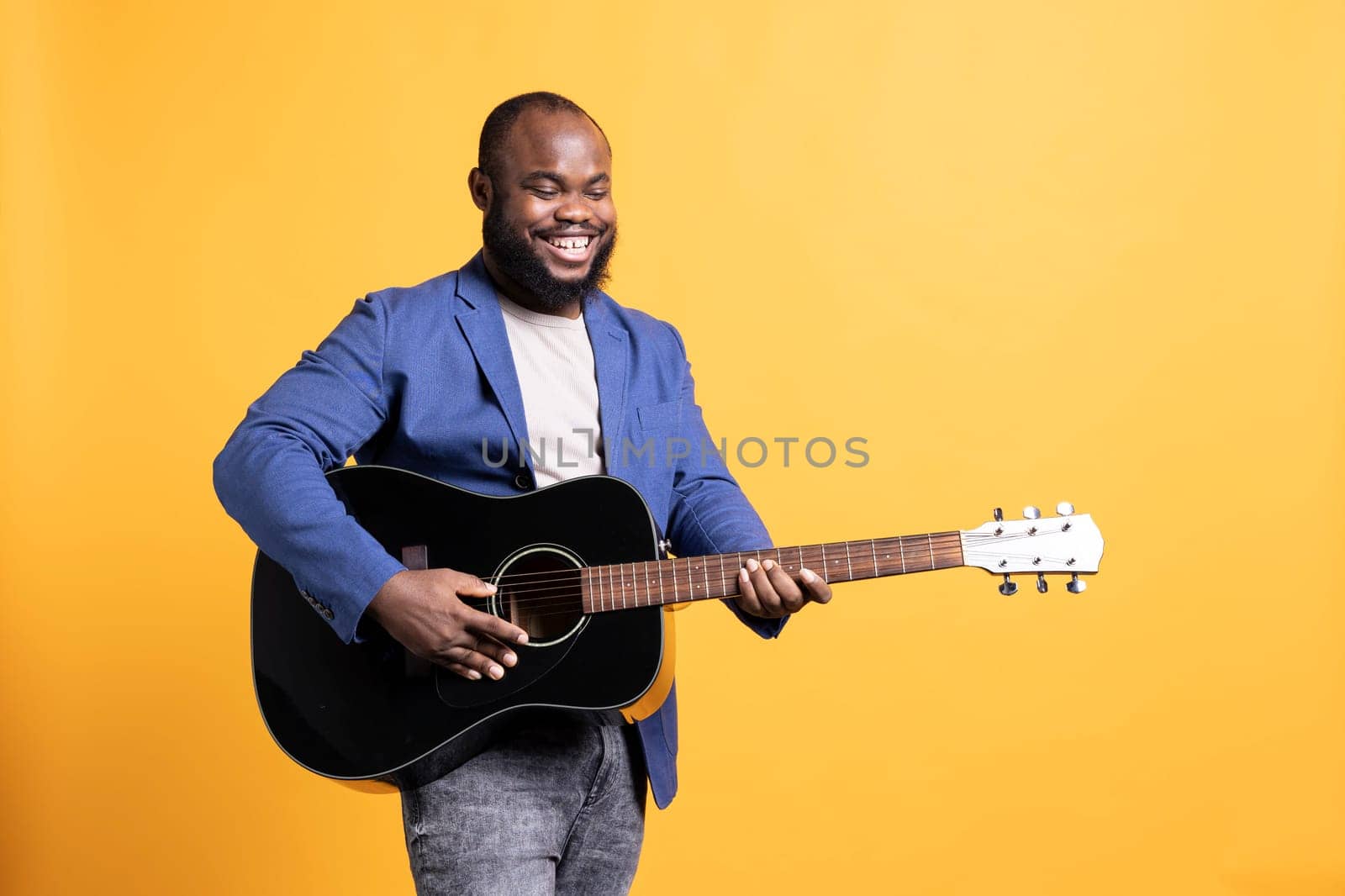 Smiling BIPOC singer holding guitar, performing blues tunes, studio background by DCStudio