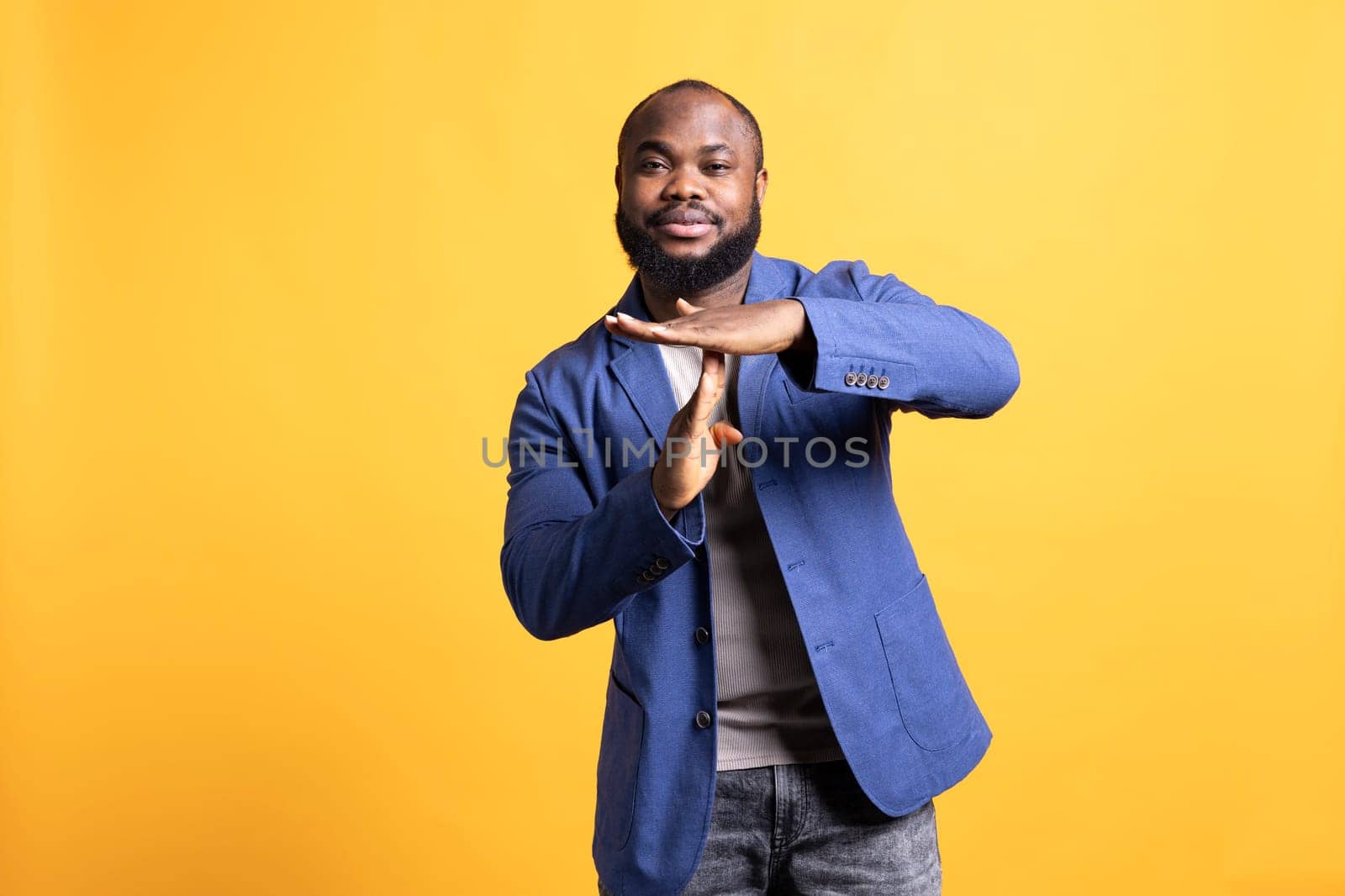 Portrait of smiling african american man asking for timeout, doing hand gestures. BIPOC person doing pause sign gesturing, wishing for break, isolated over studio background